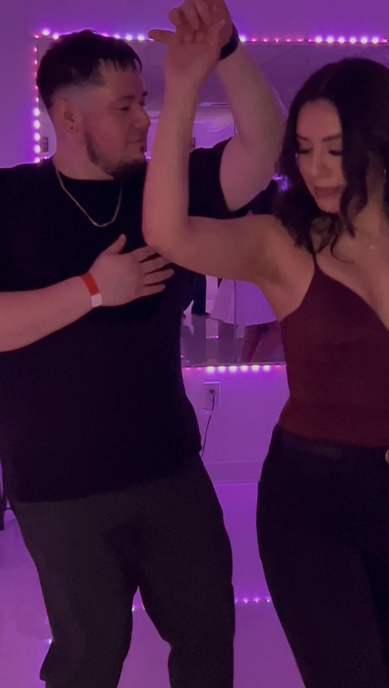 Two people dancing together in a room decorated with purple LED lights, with one person holding the other's arm in a dance pose.
