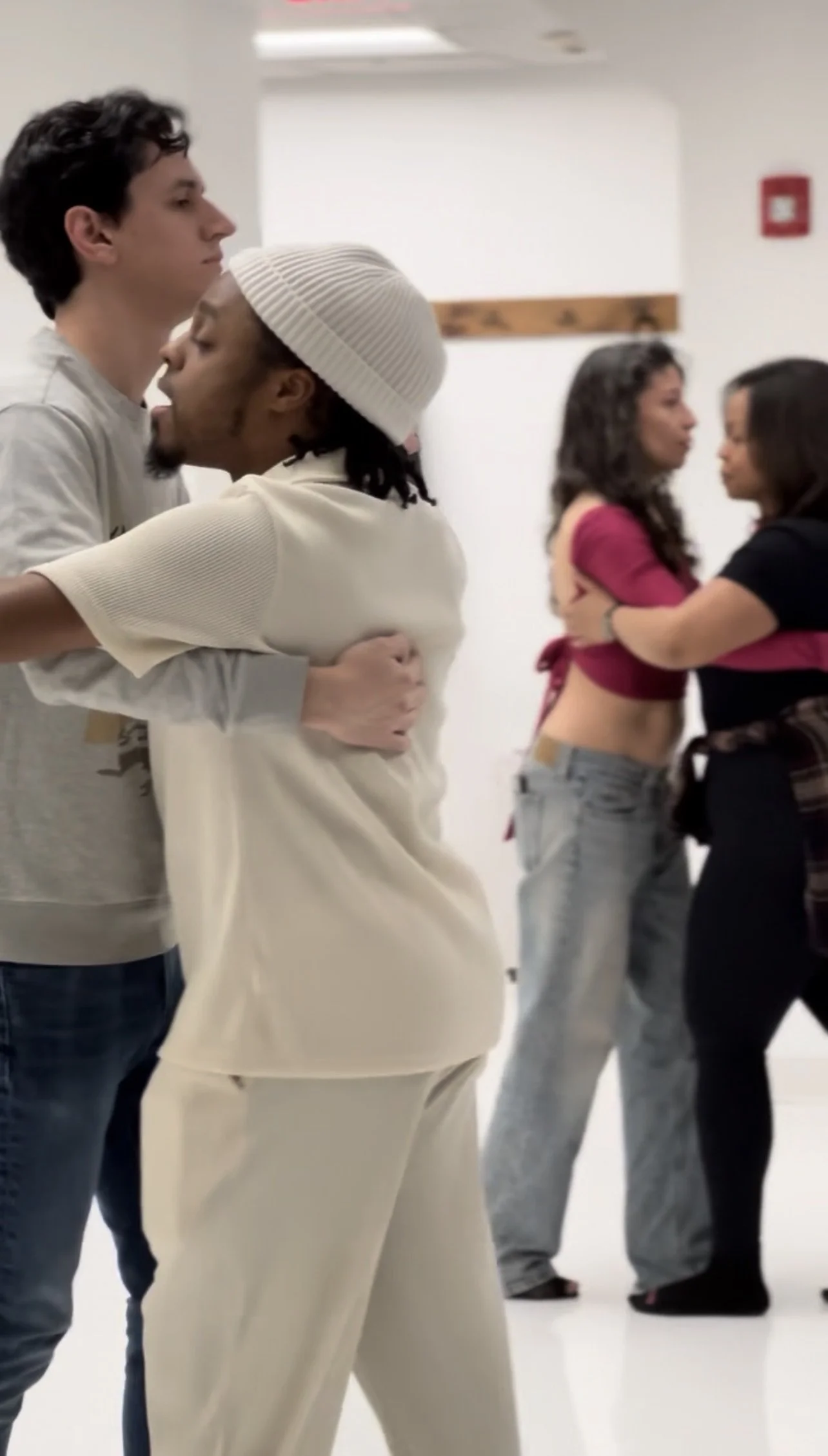 Several couples dancing closely in an indoor setting with plain white walls.