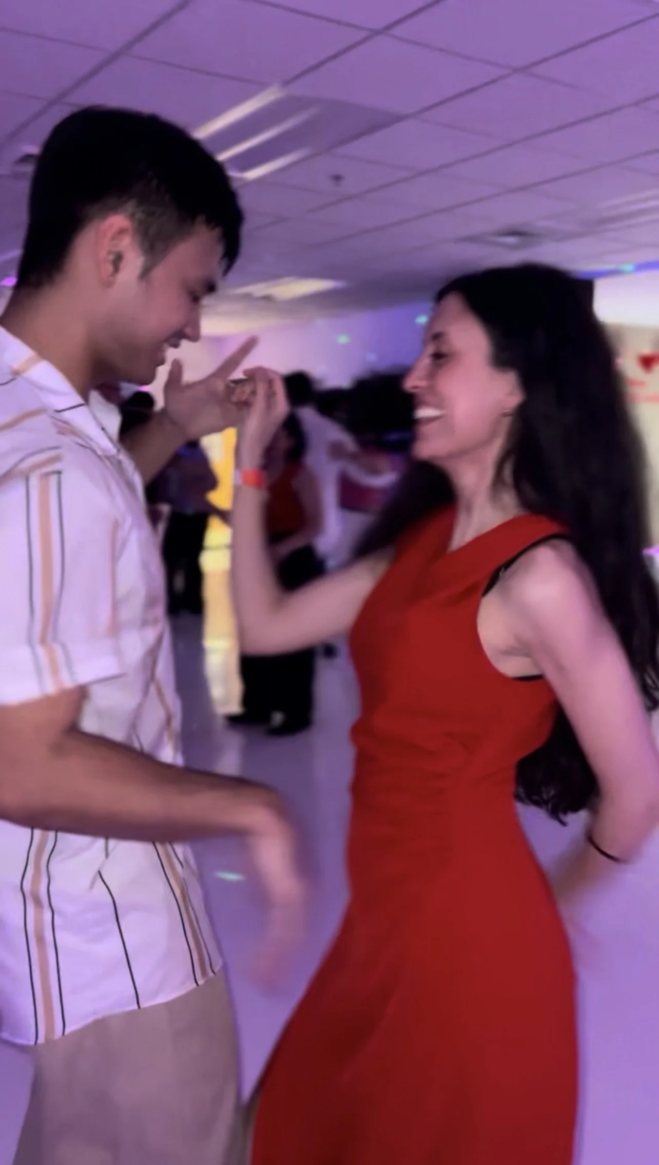 A man and a woman dancing together in a dimly lit room with purple lighting, smiling and facing each other.