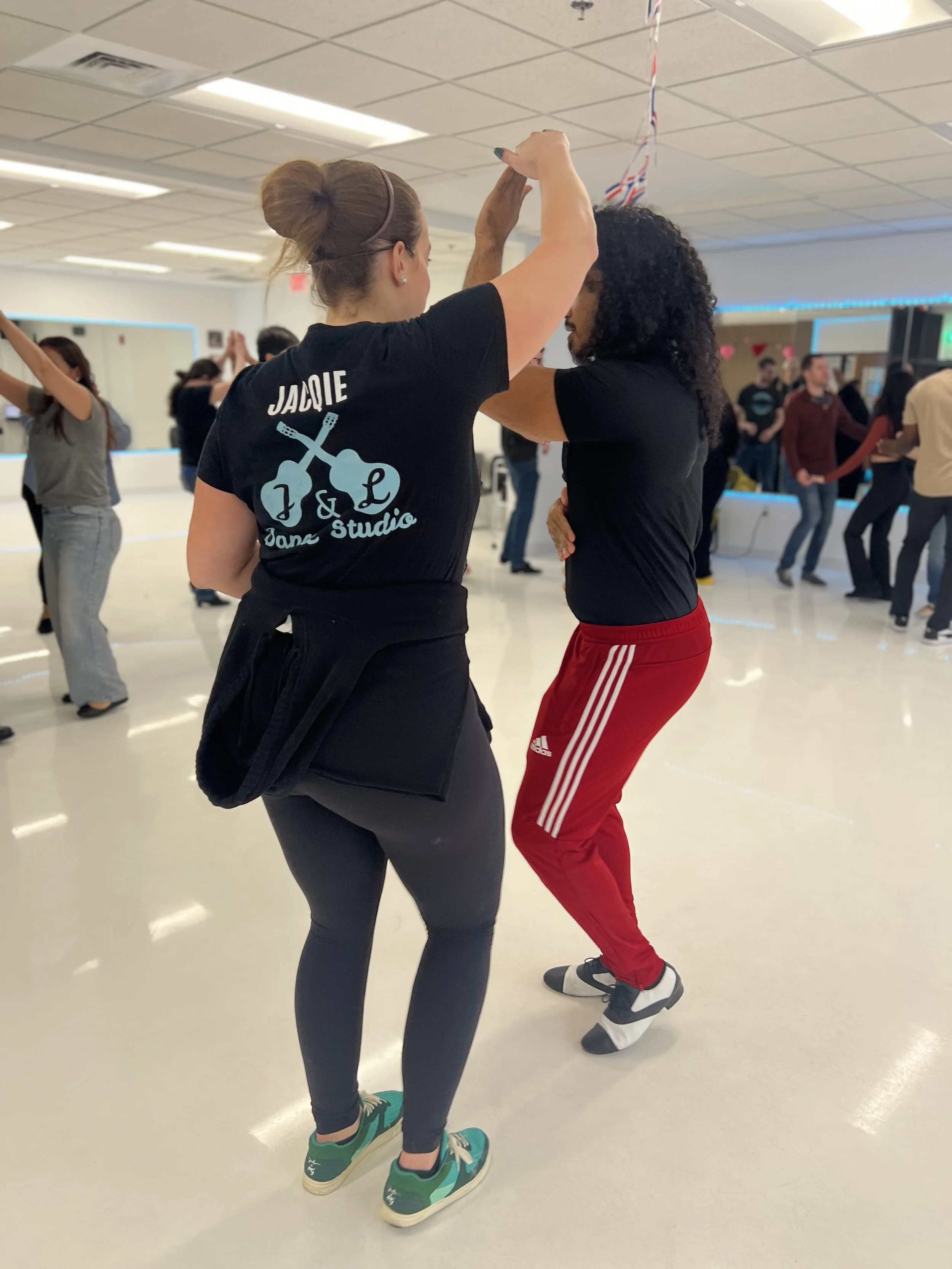 Two women dancing together in a dance studio with other couples dancing in the background.
