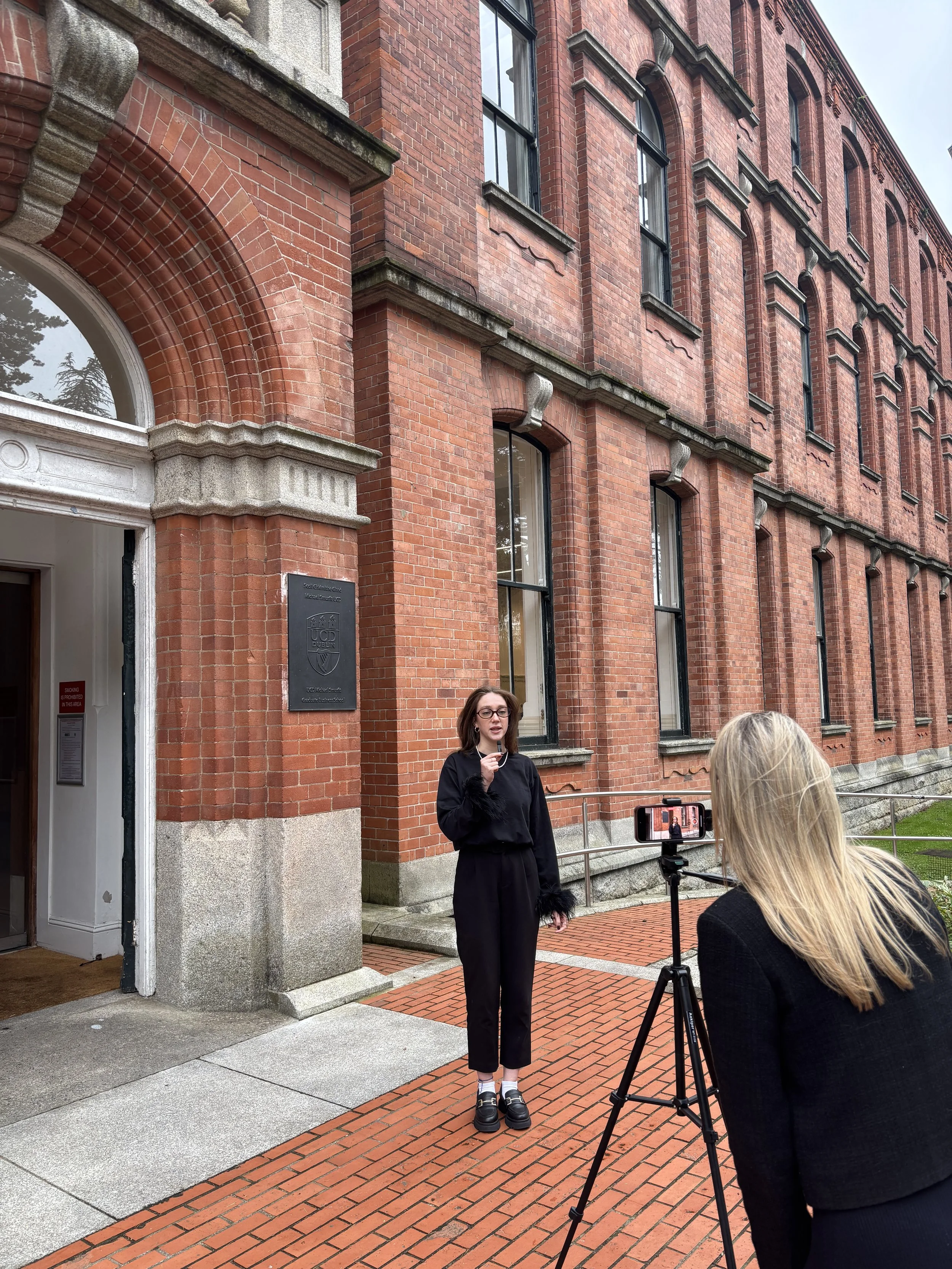 UCD Smurfit MDP student recording a video presentation outside the red-brick Graduate Business School building