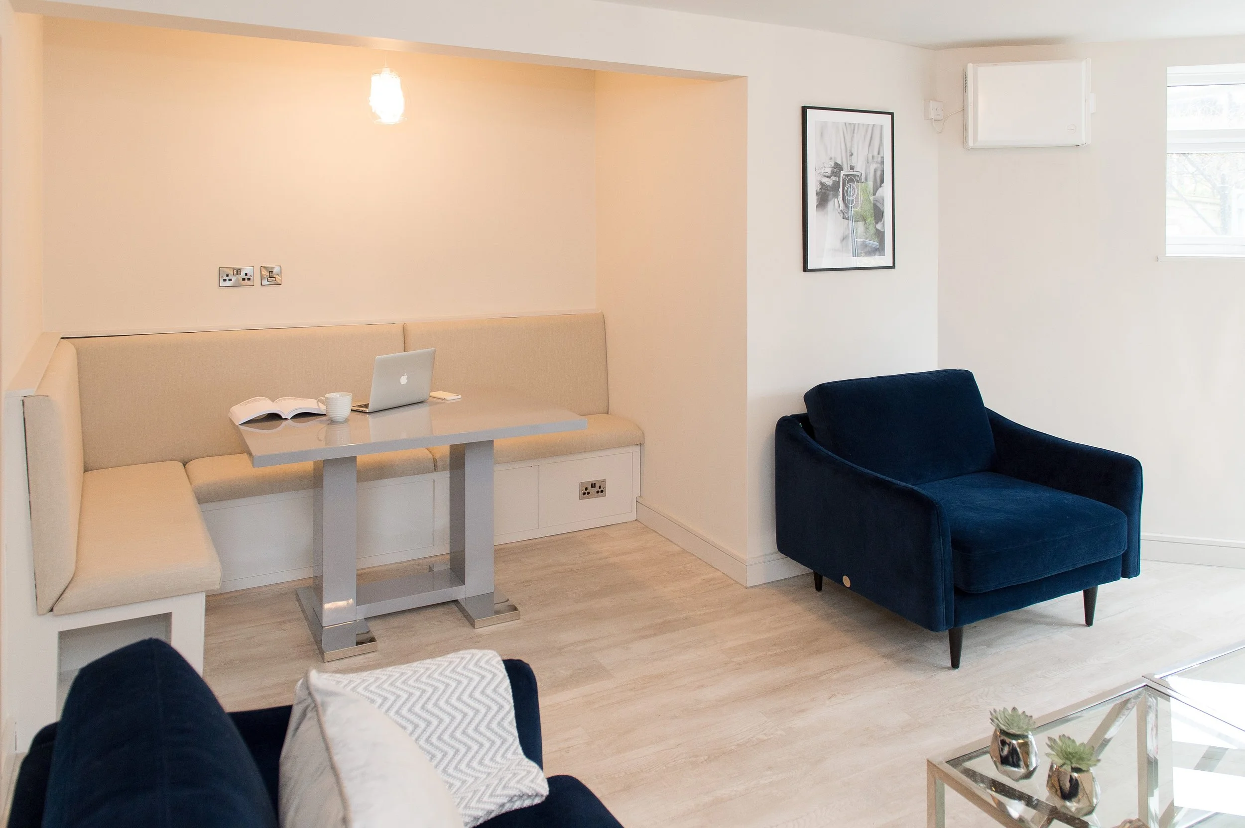 A cozy living room with white and navy blue furniture, a small table, and a picture frame on the wall, illuminated with natural light from a window.