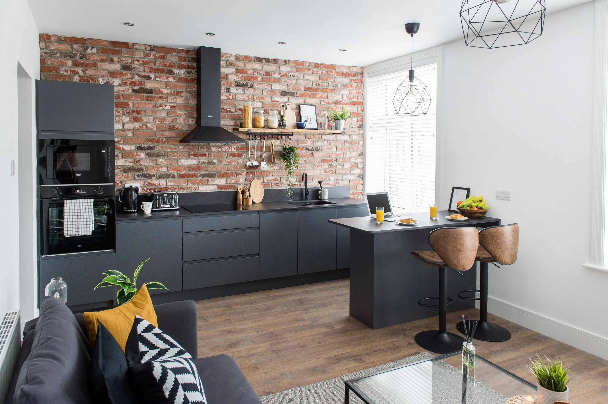 Modern kitchen with brick wall, black cabinetry, and a dining area with glasses of orange juice and bananas on the table.