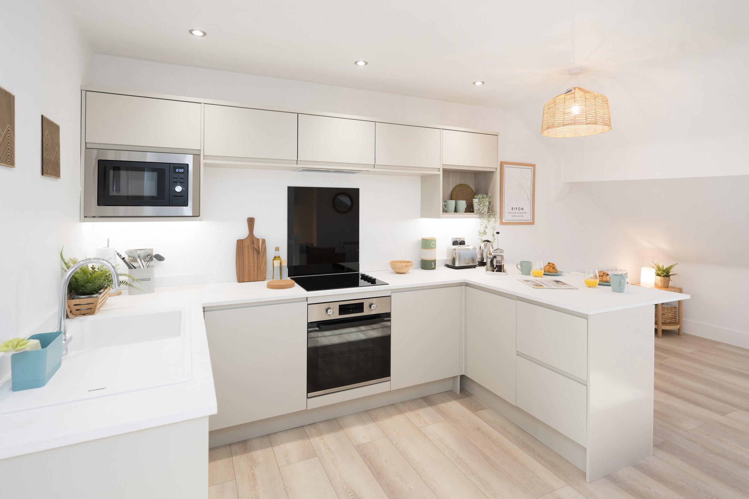 Modern white kitchen with built-in microwave, oven, and small kitchen appliances on the counter, decorated with plants and framed artwork.