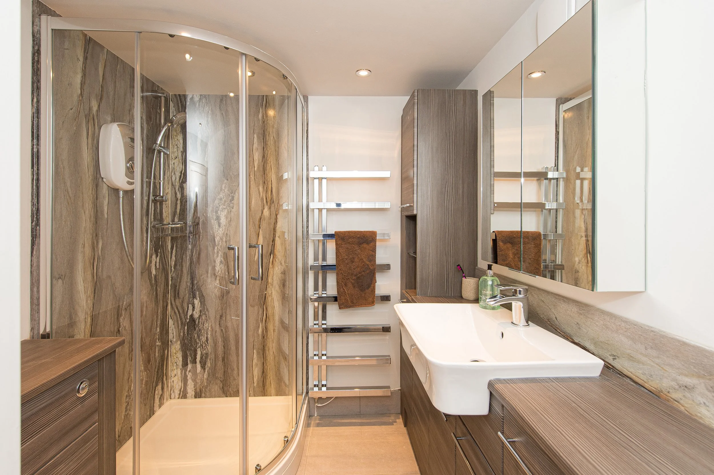 Modern bathroom with marble accents, glass shower enclosure, white sink, mirror, towel rack, and wooden accents.