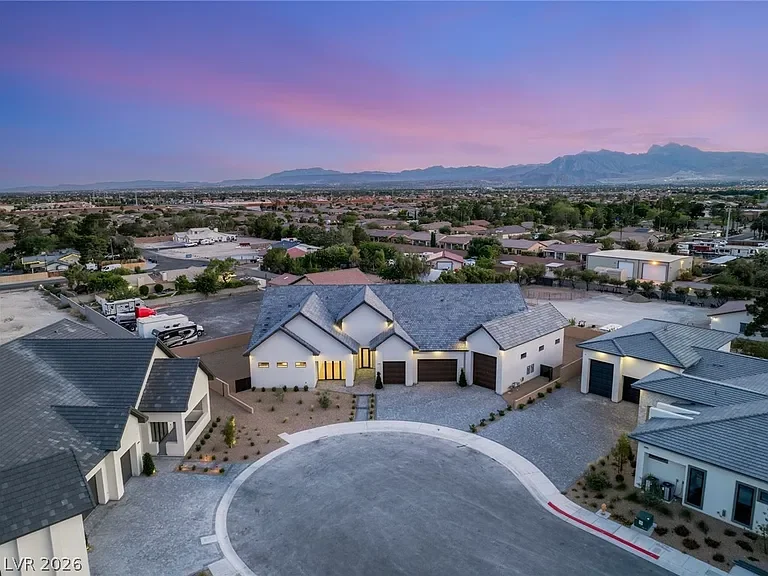 Aerial view of a residential neighborhood at sunset with modern houses, a circular driveway, and mountains in the background.