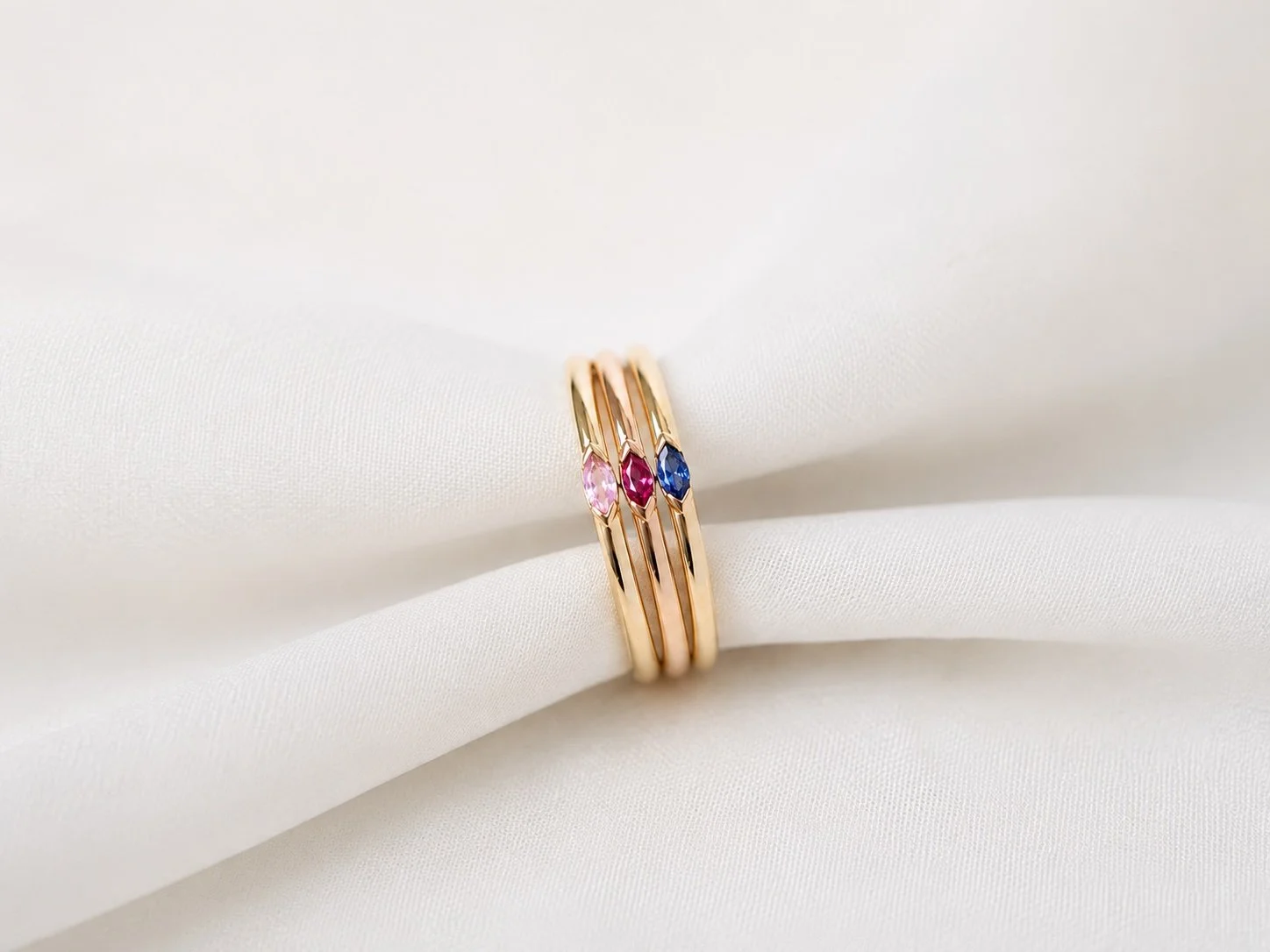 Zarte goldene Ringe mit pinkem, rotem und blauem Edelstein auf weißem Stoff