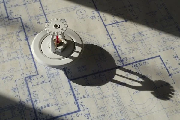 A mechanical timer placed on architectural blueprints, casting a shadow.