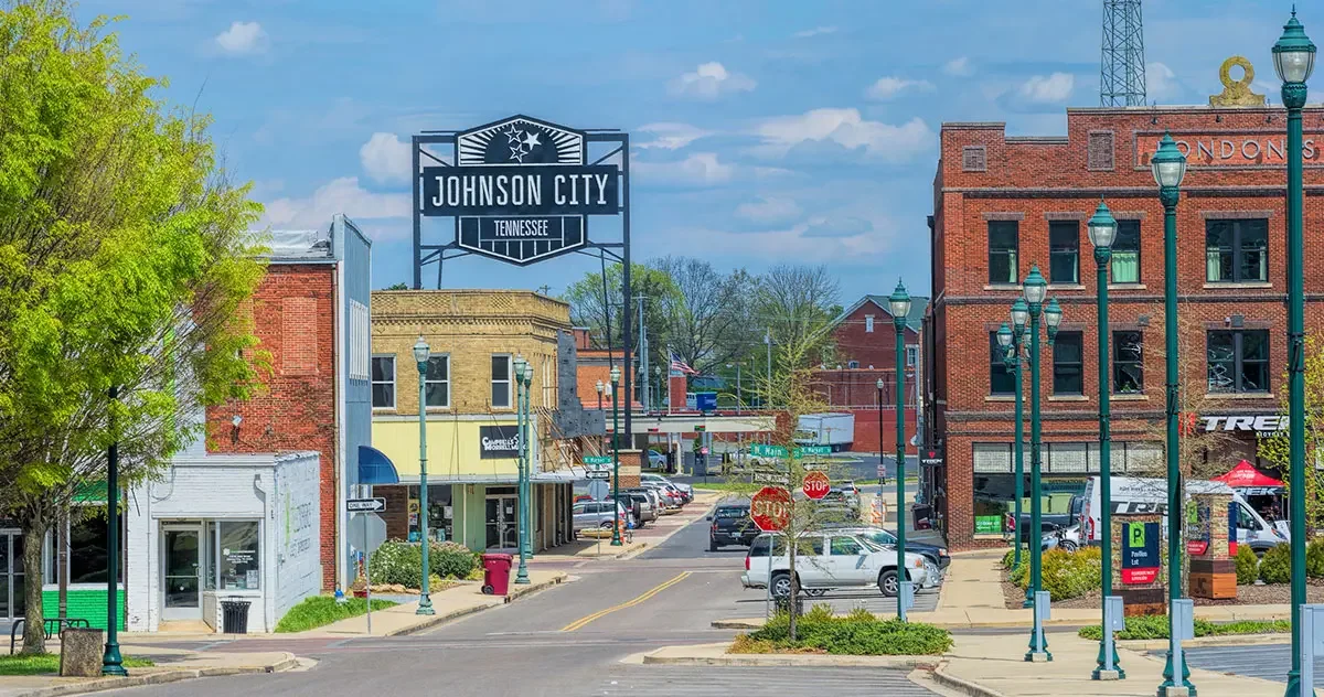 Downtown Johnson City, Tennessee with historic brick buildings, parking meters, street lamps, stop signs, and a large sign overhead.