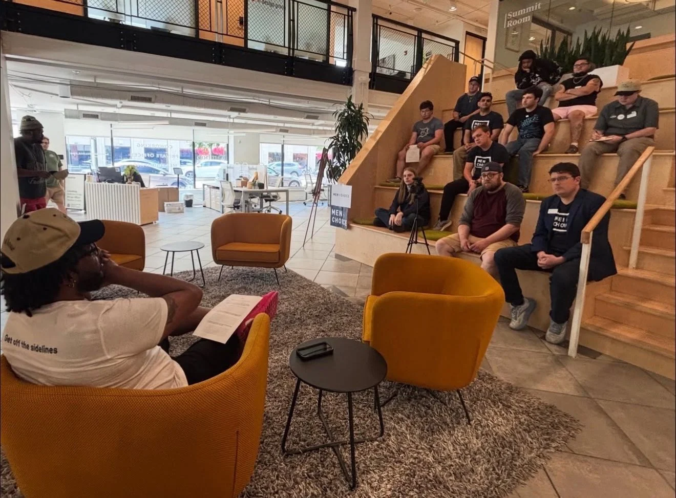 DeNiro Jones facilitating a Men4Choice action session with participants gathered in a community meeting space.