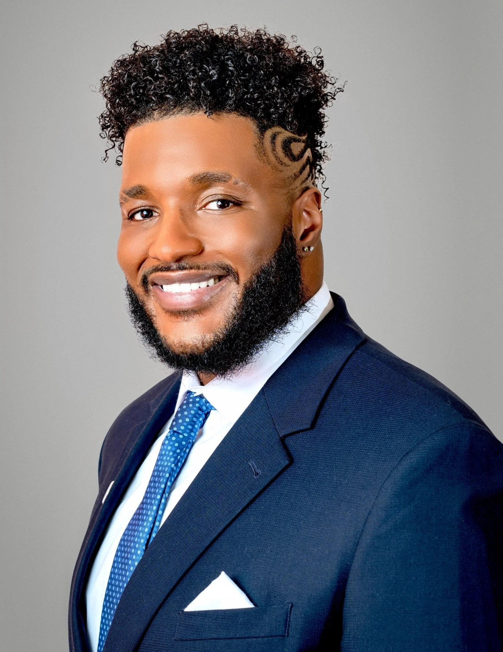 Professional portrait of DeNiro Jones wearing a navy suit and blue tie.