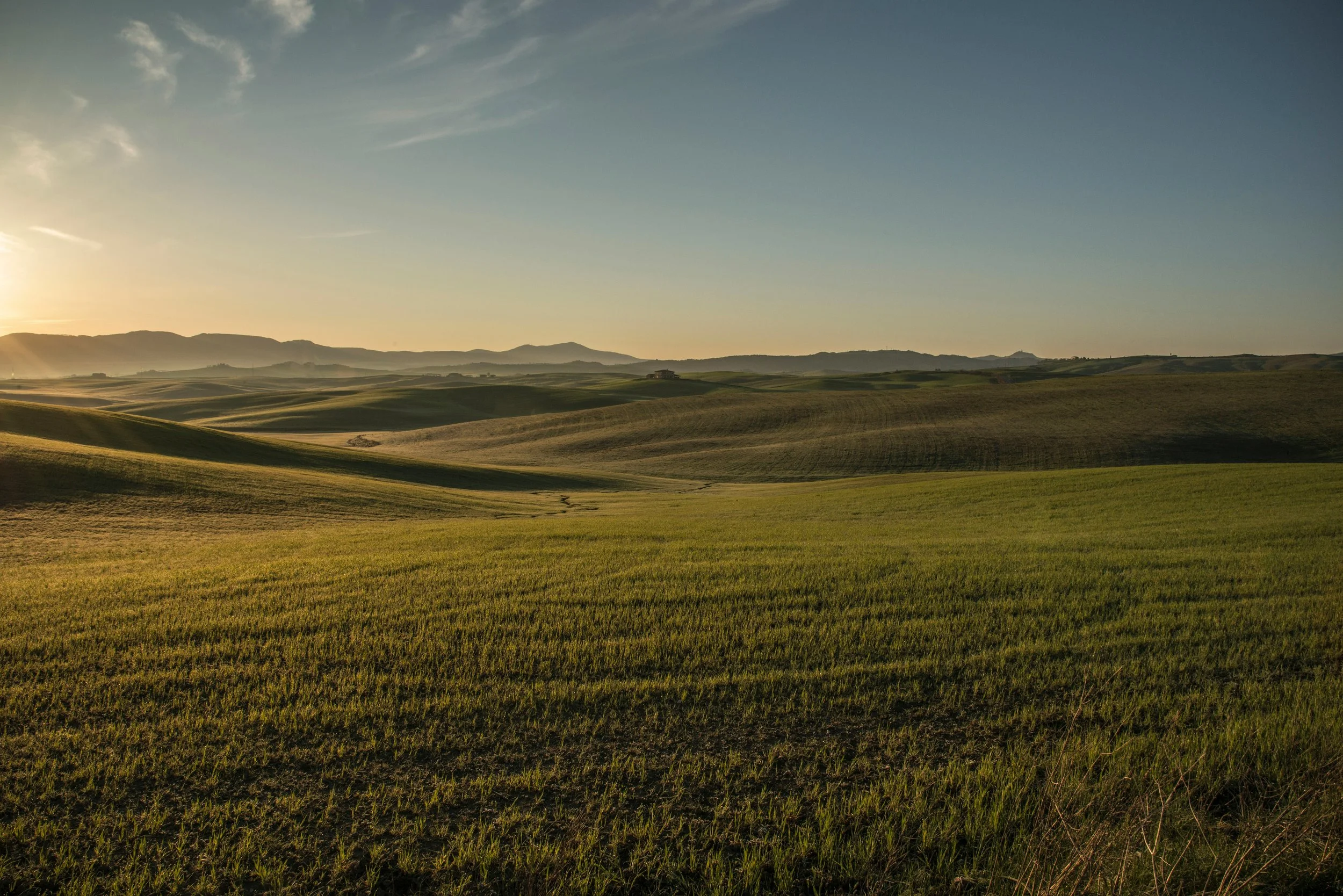 Sunset over rolling green fields with distant hills and a clear sky.
