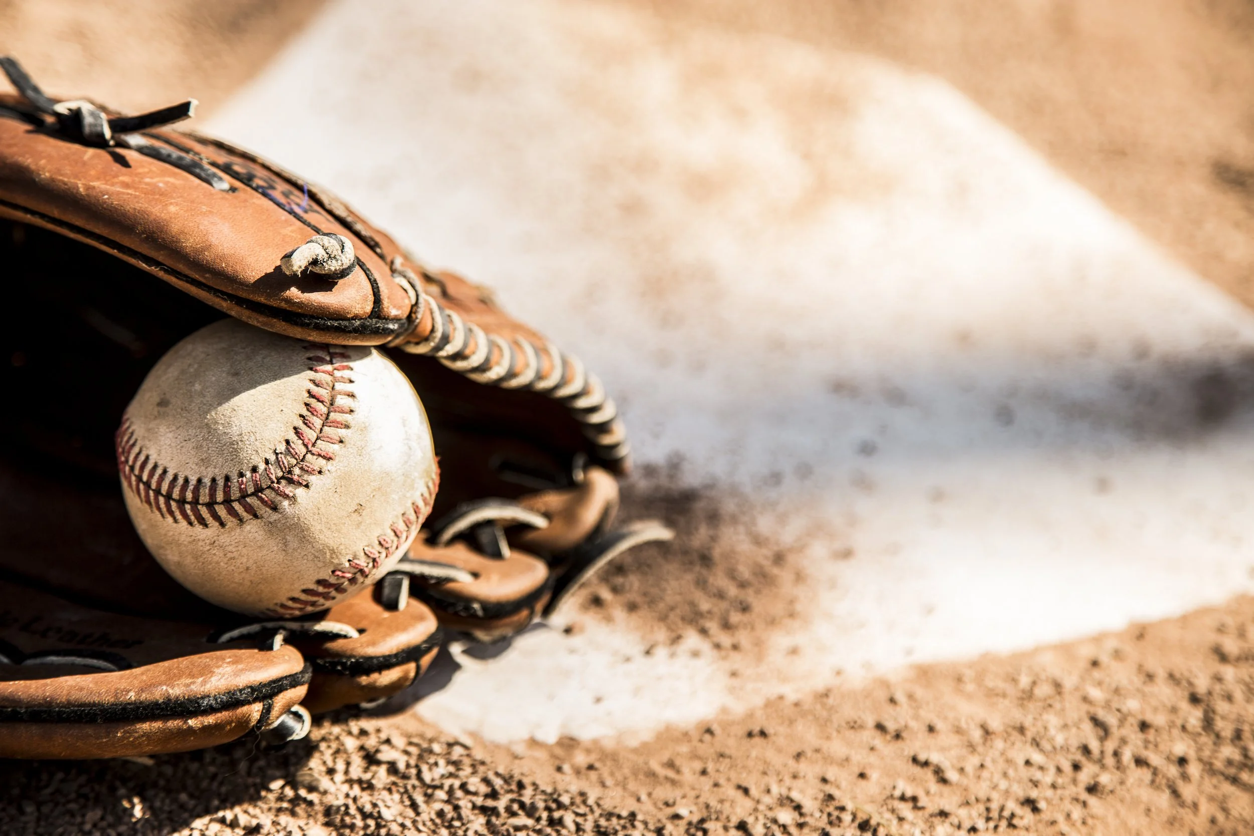 A worn baseball glove holding a baseball on a dirt ground.