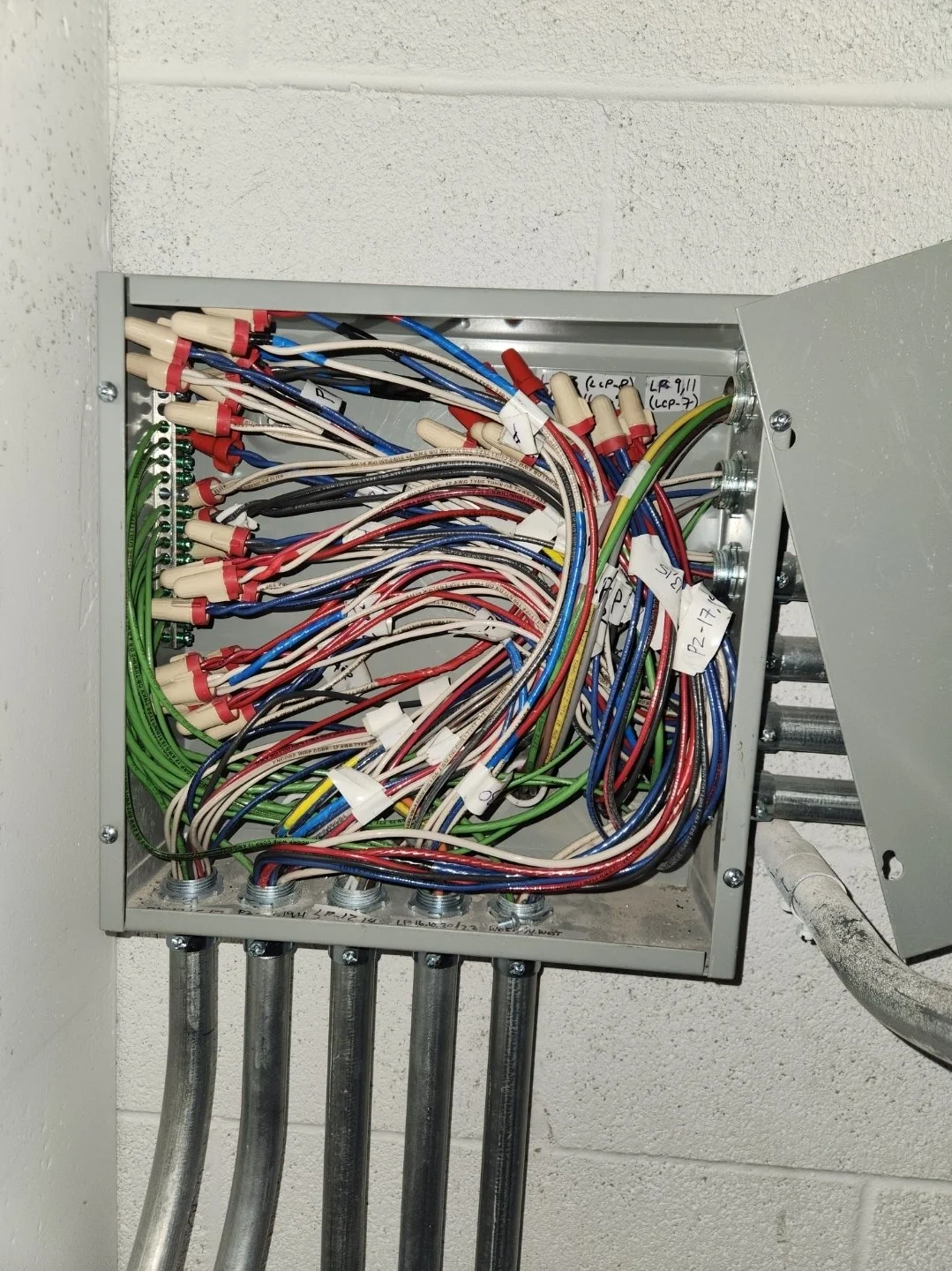 Electrical panel with multiple colored wires and labels mounted on a wall.