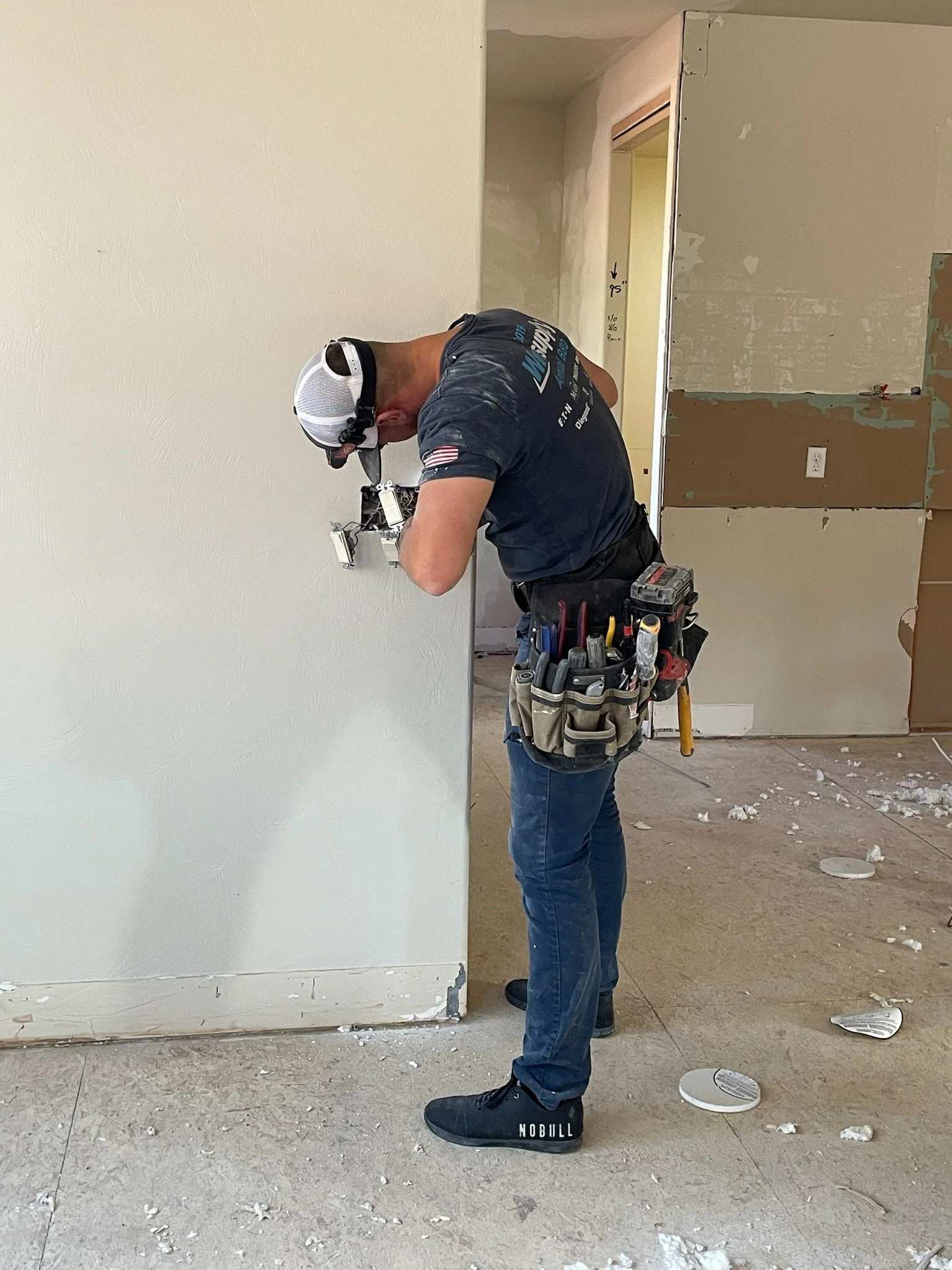 Construction worker installing electrical wiring inside a metal electrical panel on a wall.