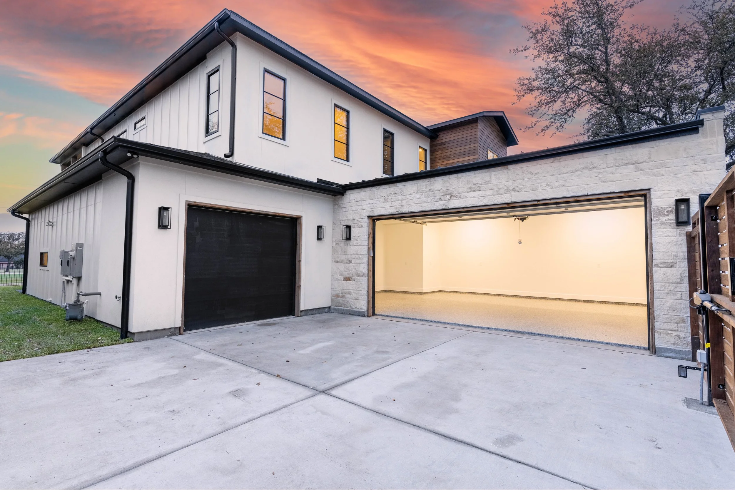 Modern white custom home at dusk with an illuminated two-car garage, concrete driveway, and landscaped front yard.