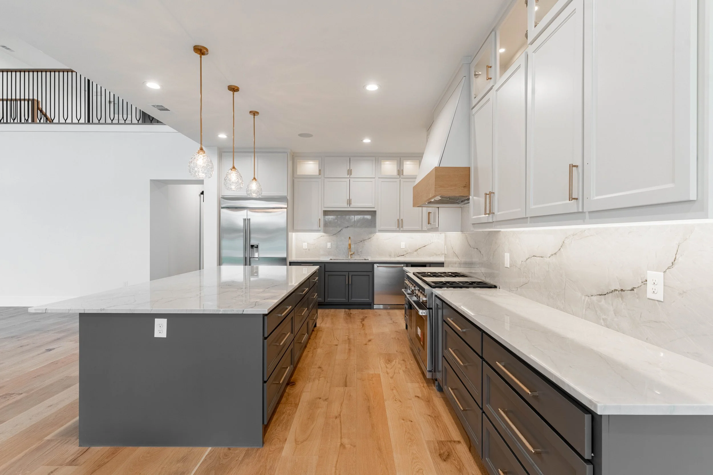 Bright custom kitchen with white cabinetry, a large island, pendant lights, and wood flooring.