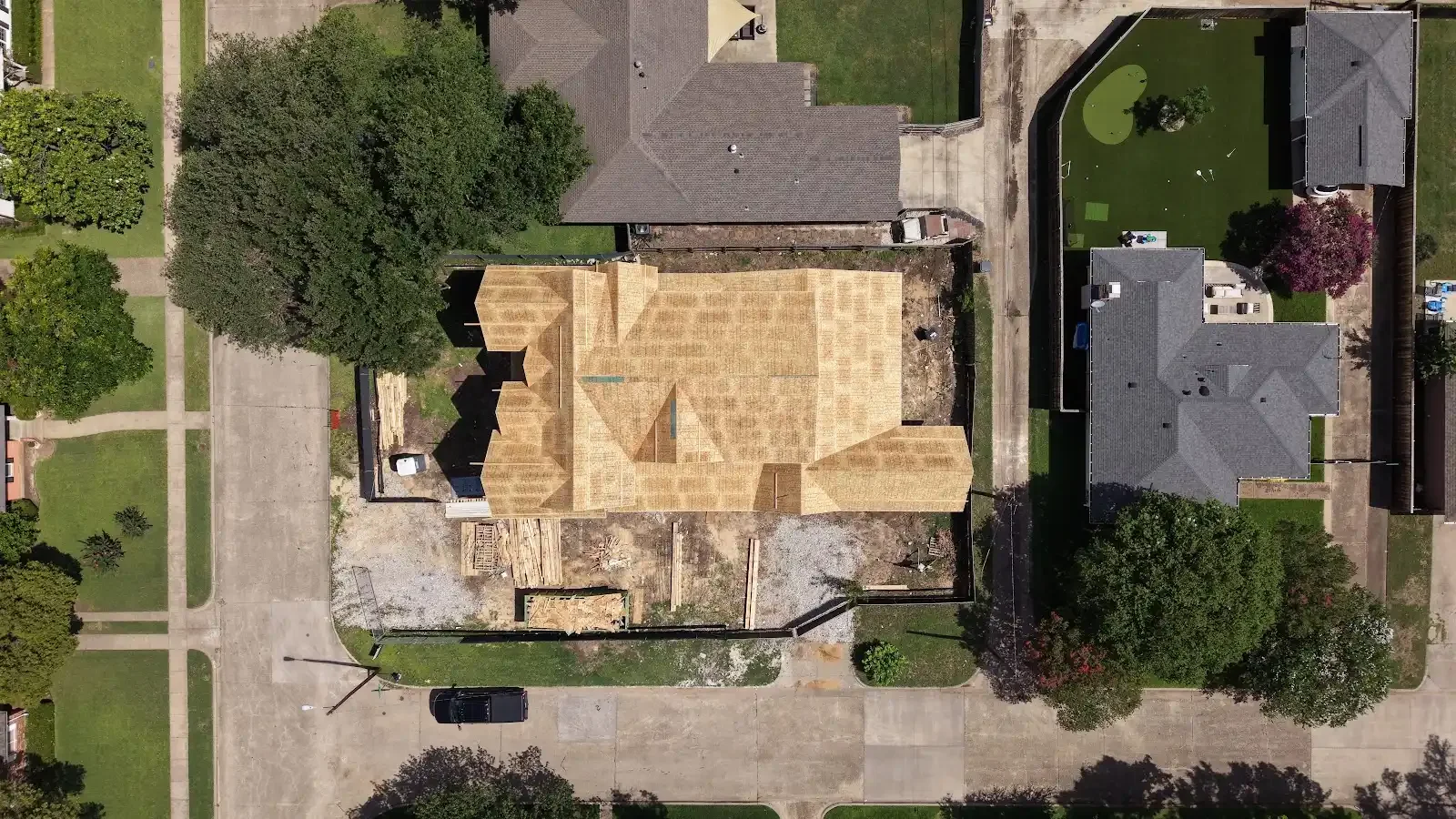 Overhead view of a custom home under construction, showing roof framing, the surrounding lot, and driveway.