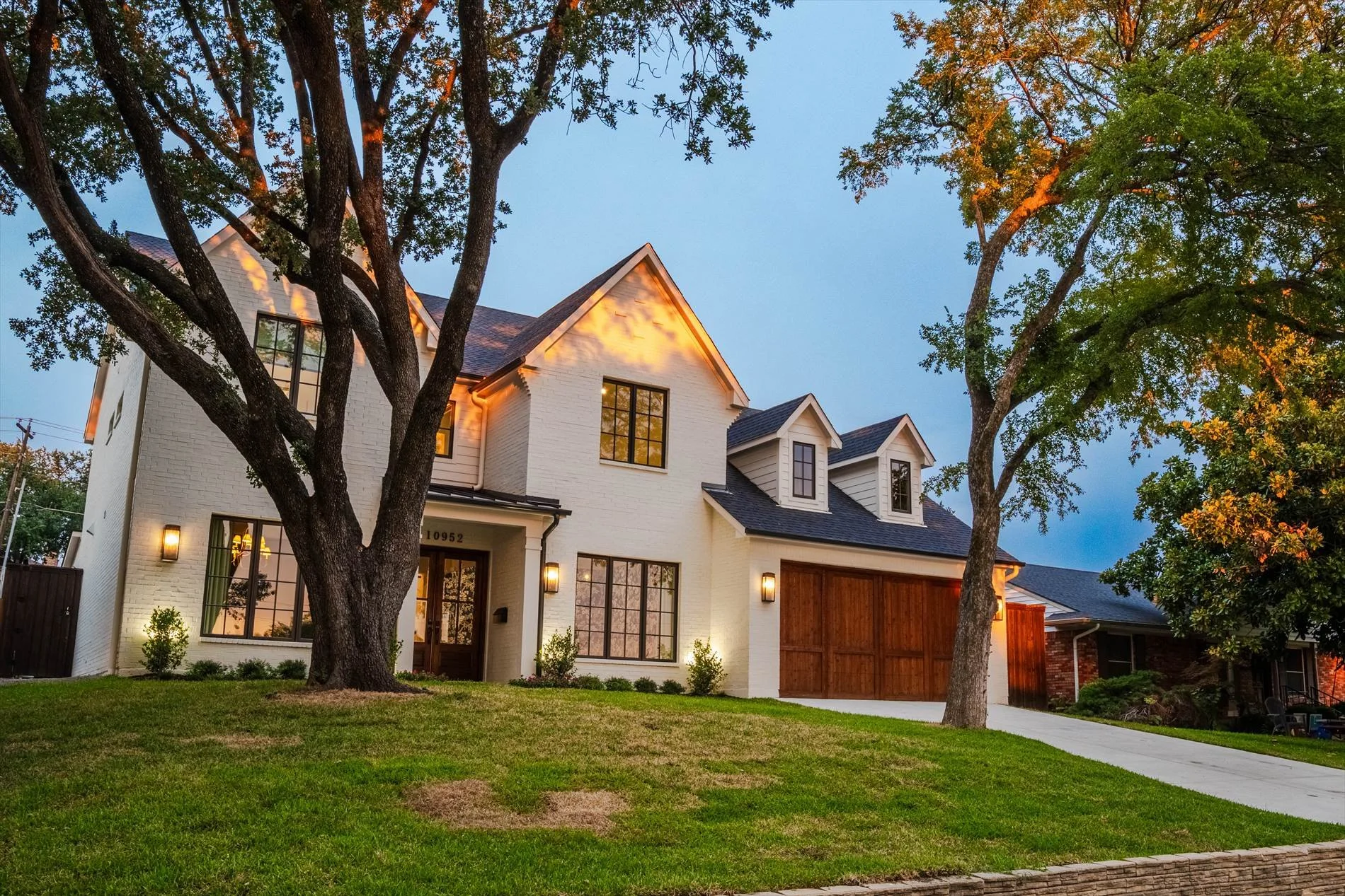 White custom home exterior with mature trees, a front lawn and wood garage doors at 1095 Lathrop Dr.
