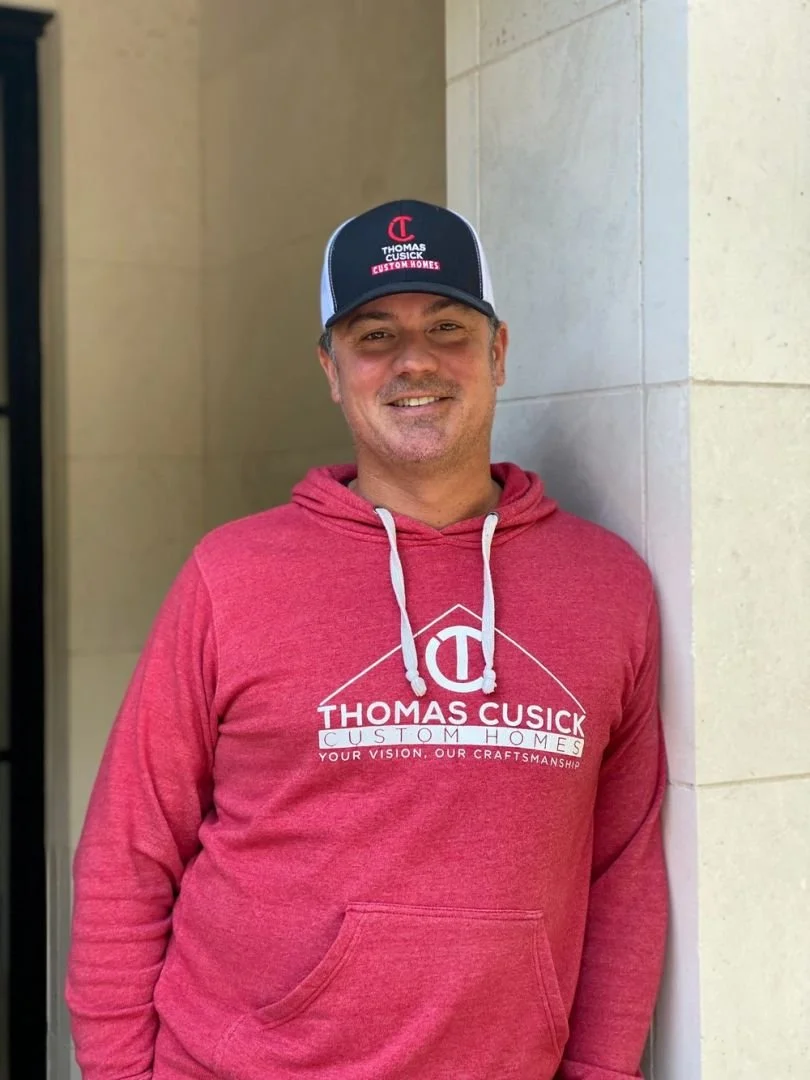 Portrait of Tom Cusick wearing a Thomas Cusick Custom Homes cap and sweatshirt.
