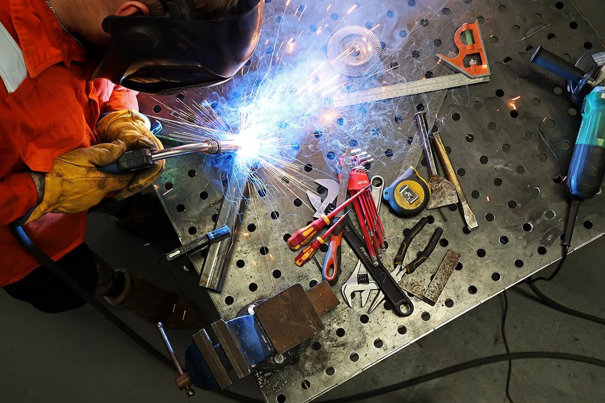 Professional welder carrying out MIG welding on a steel fabrication workbench with welding sparks.