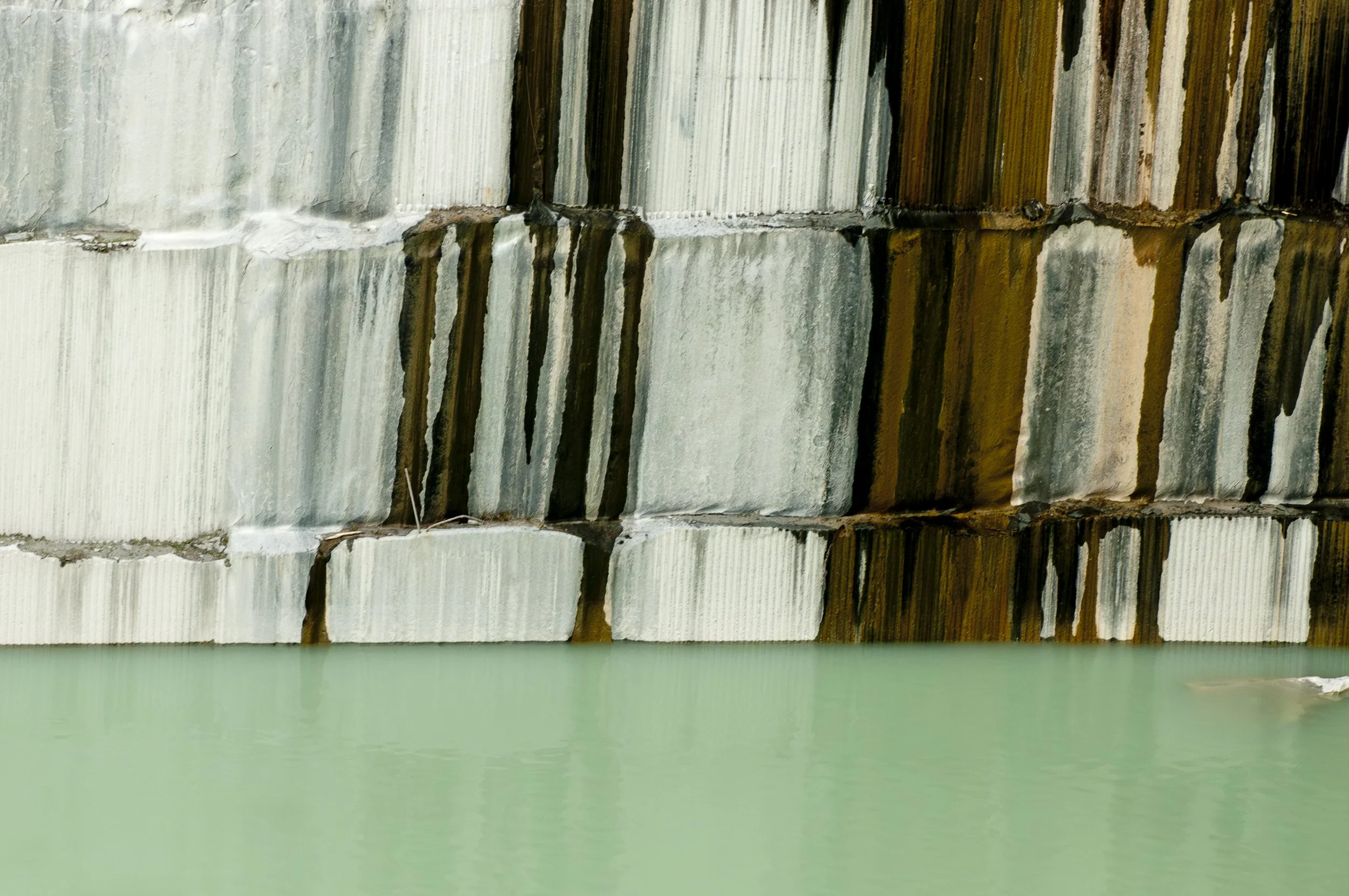 Close-up photo of a concrete dam with water flowing over the edge, creating a waterfall-like effect with reflected water below.
