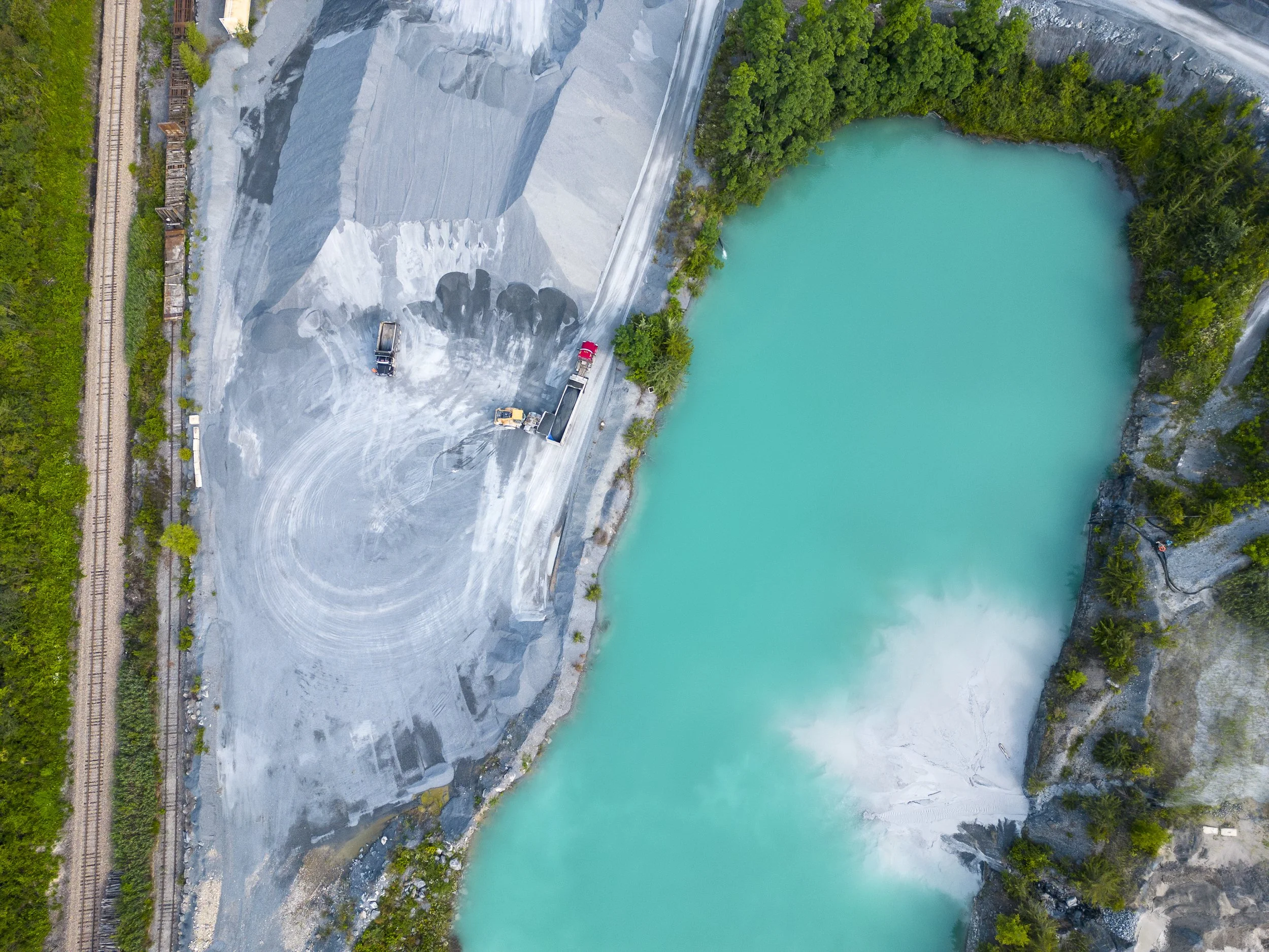 An aerial drone photo of a turquoise body of water surrounded by green trees and a quarry.