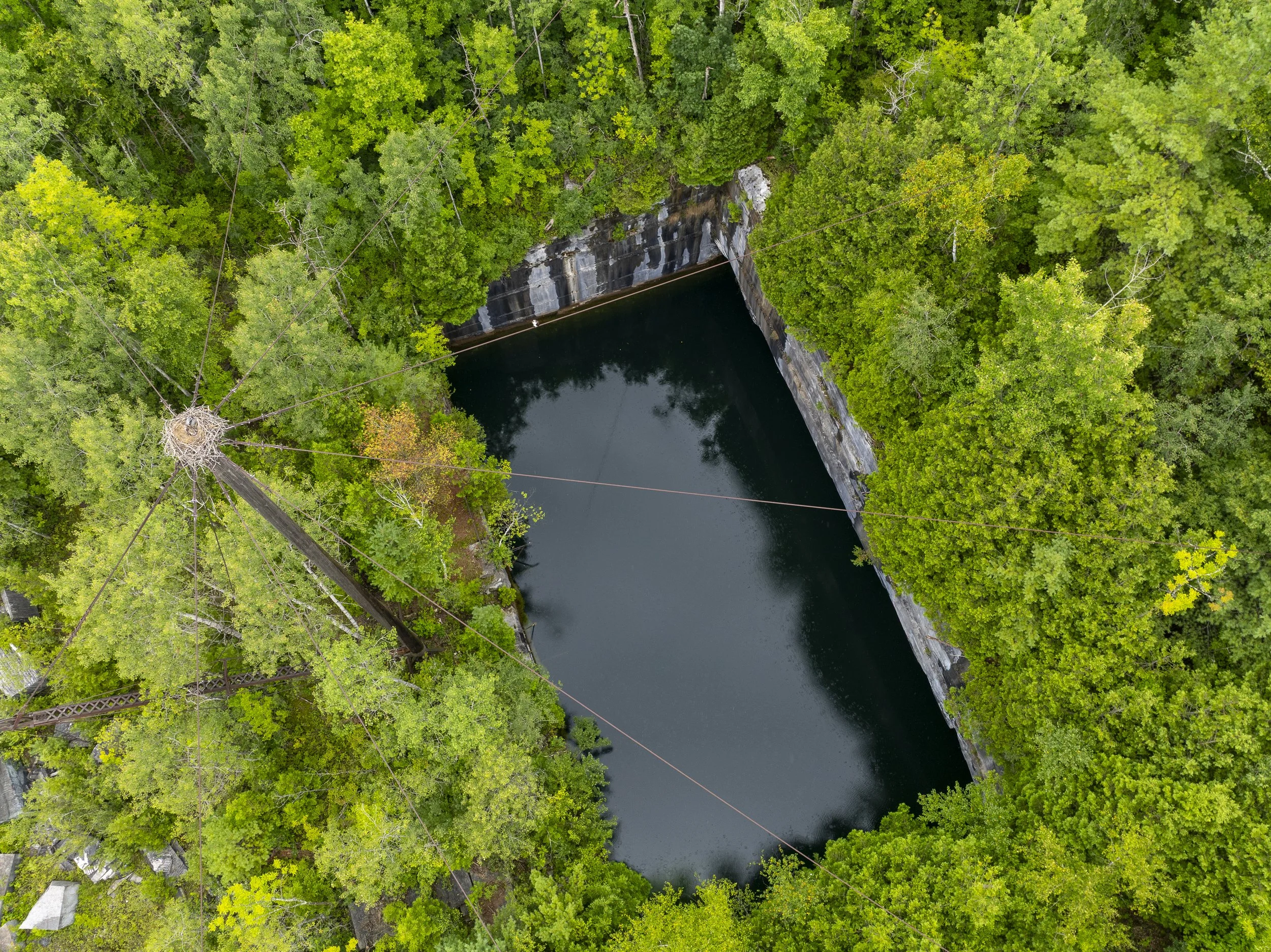 An aerial view photo of a quarry surrounded by dense green forest and a body of water below.
