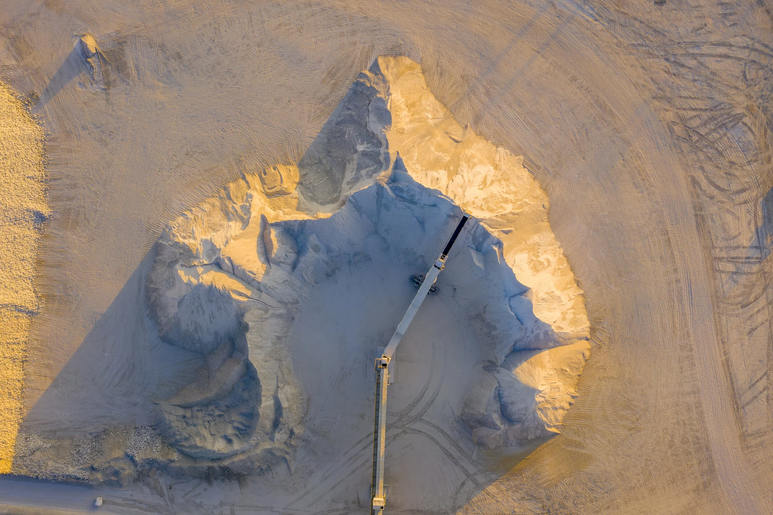 An aerial view photo of a large snow-covered quarry with a crane extending across it. 