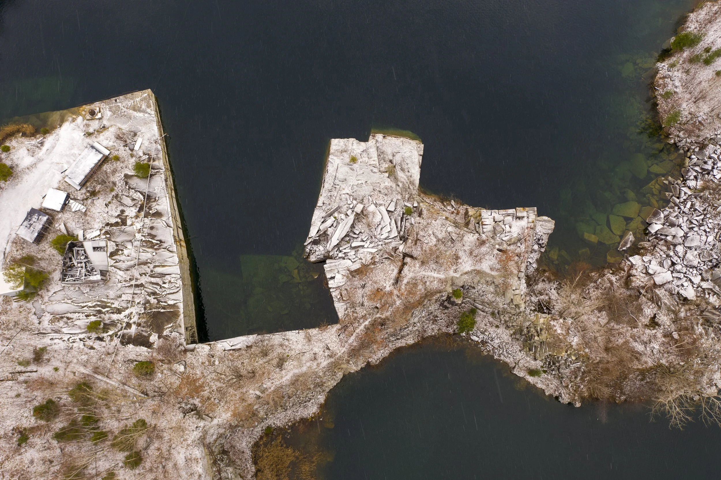 An aerial view of a quarry with a body of water with rocky shores and some greenery.