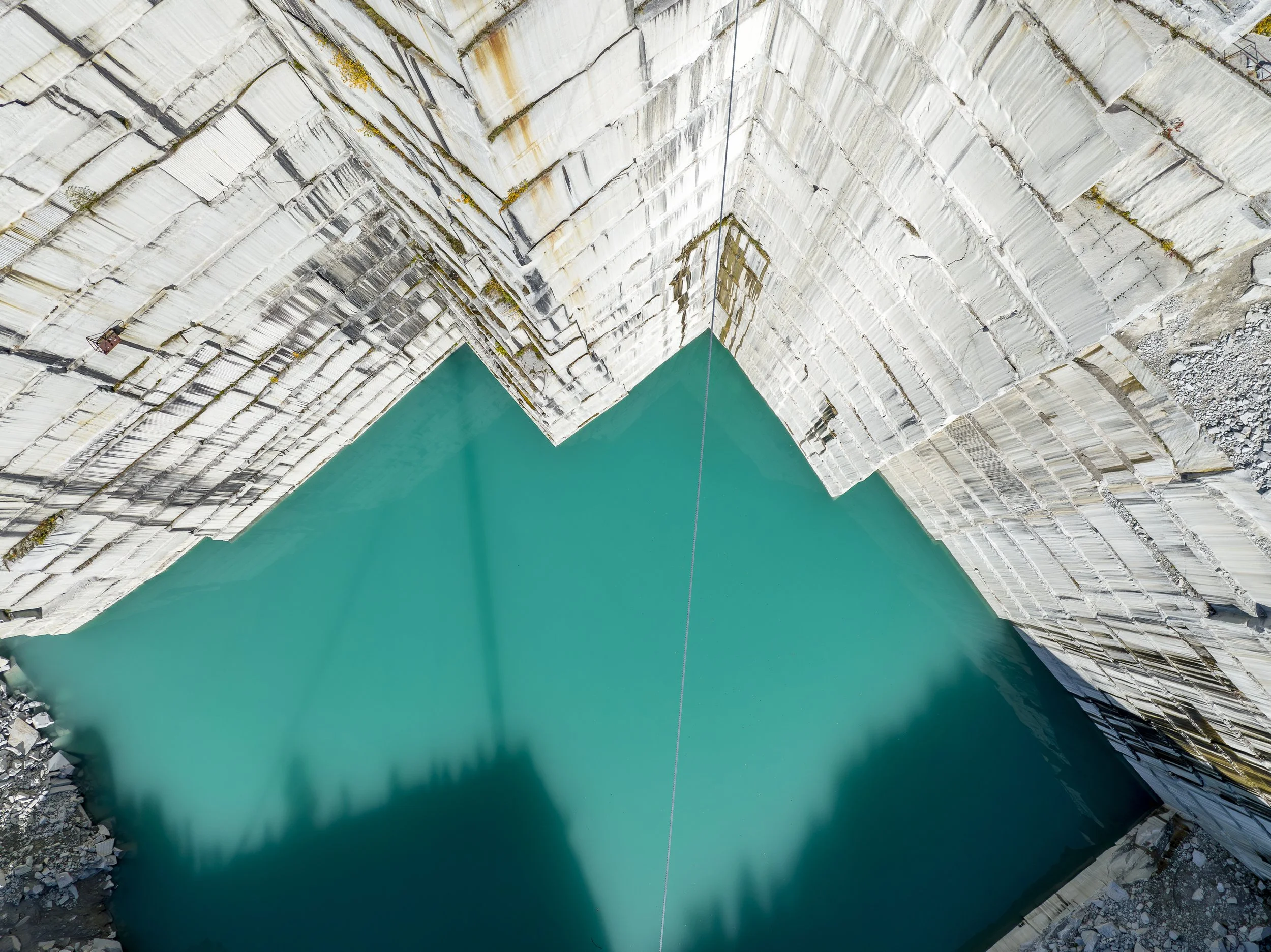 Aerial drone photography of a large quarry with turquoise water below.
