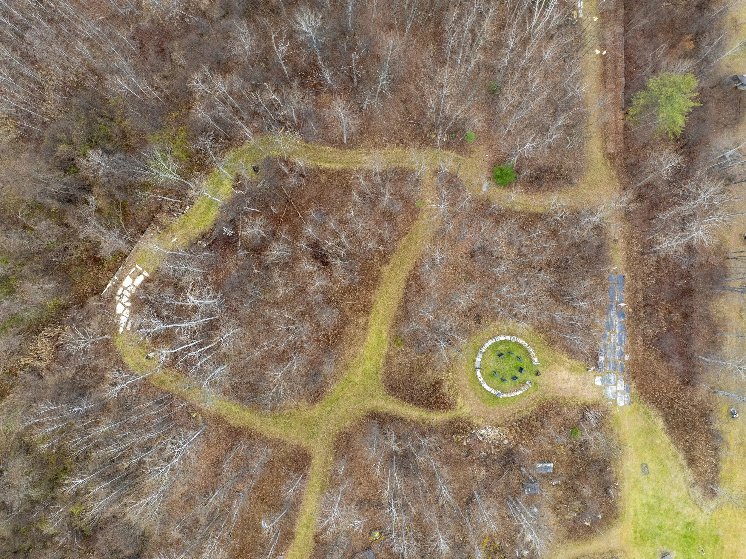 Aerial landscape photo of a park with leafless trees, grassy paths, and a circular flowerbed with plants and benches, during fall or winter in Vermont.