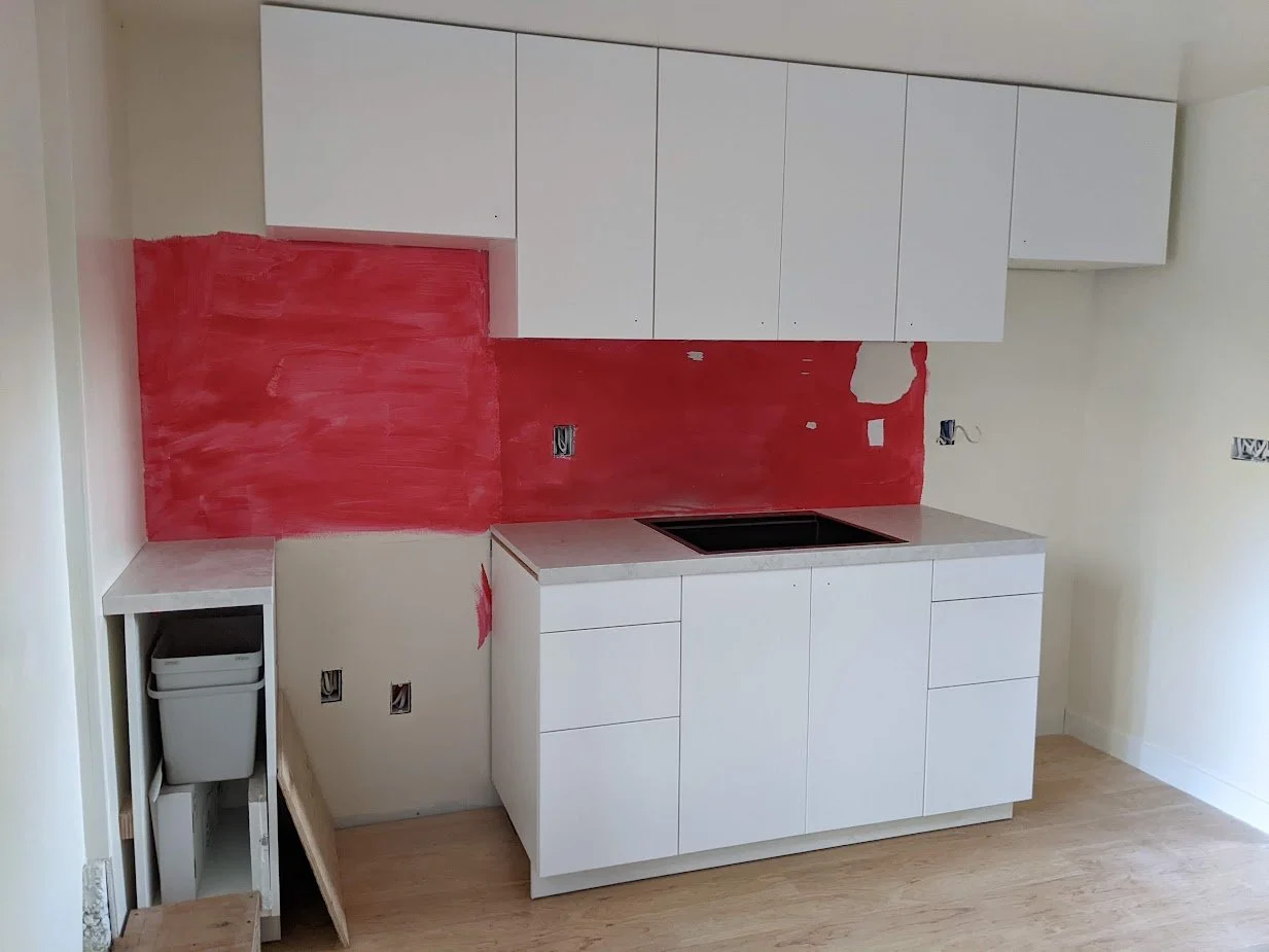 Kitchen under construction with white cabinets, red wall paint, and a black sink, with unfinished walls and wiring.