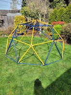 A colorful outdoor playground structure resembling a dome made of yellow, blue, and red bars on a grassy yard.