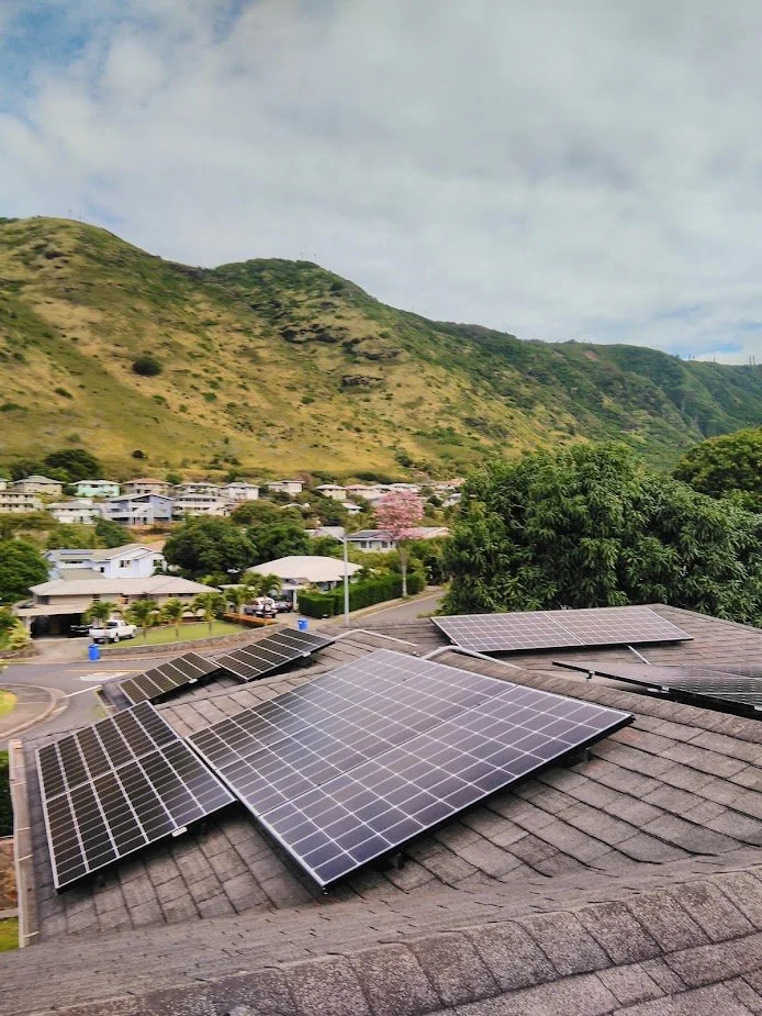 Solar panels installed on the roof of a house with green hills and a neighborhood in the background.