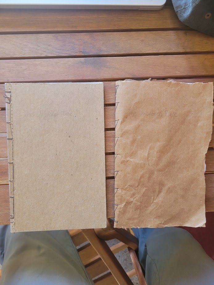 Two sheets of paper, one plain and the other crumpled, placed on a wooden surface next to a laptop and person's legs.