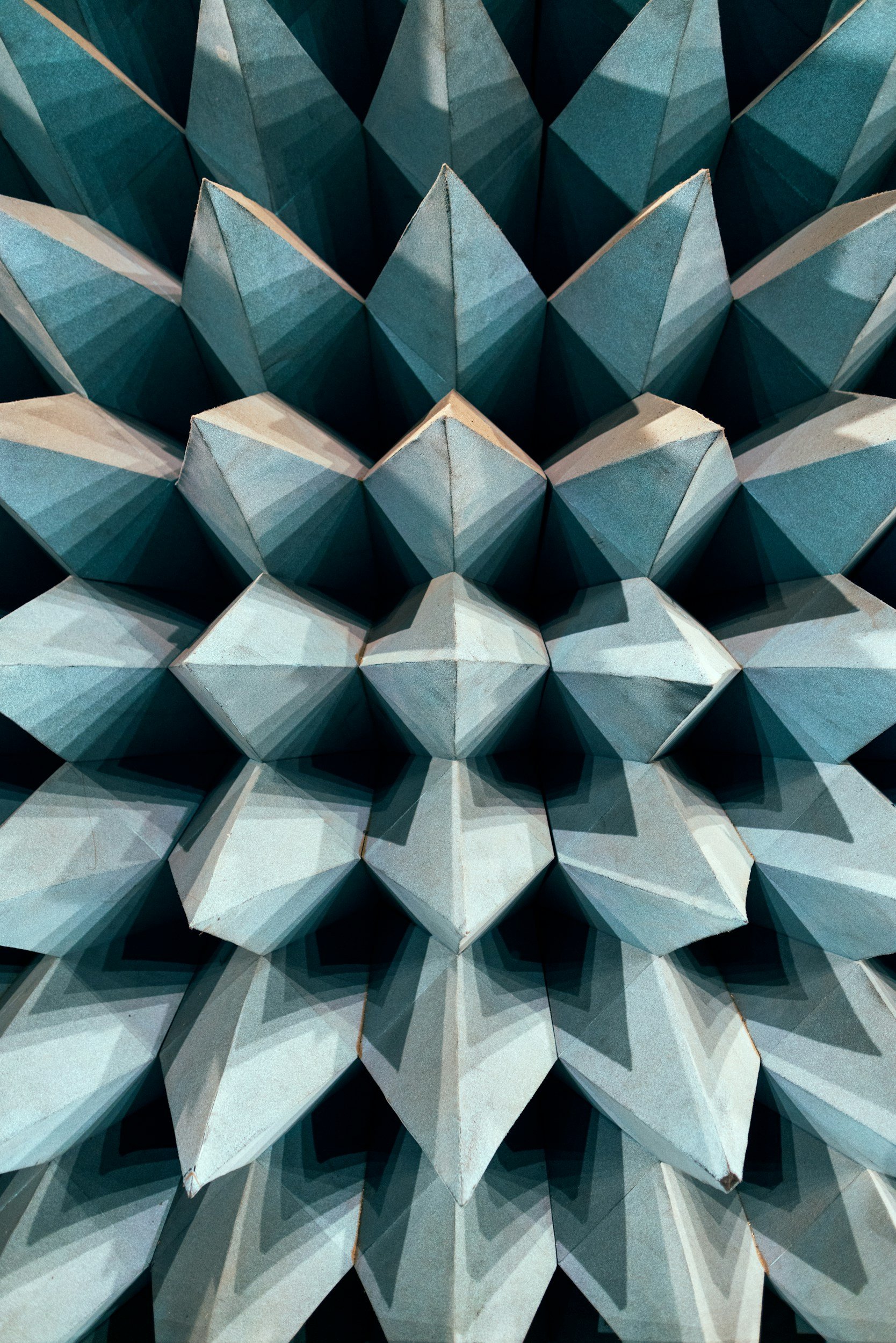 Close-up view of a geometric wall art sculpture made of folded paper or cardboard arranged in a repetitive triangular pattern with shades of blue, gray, and white.
