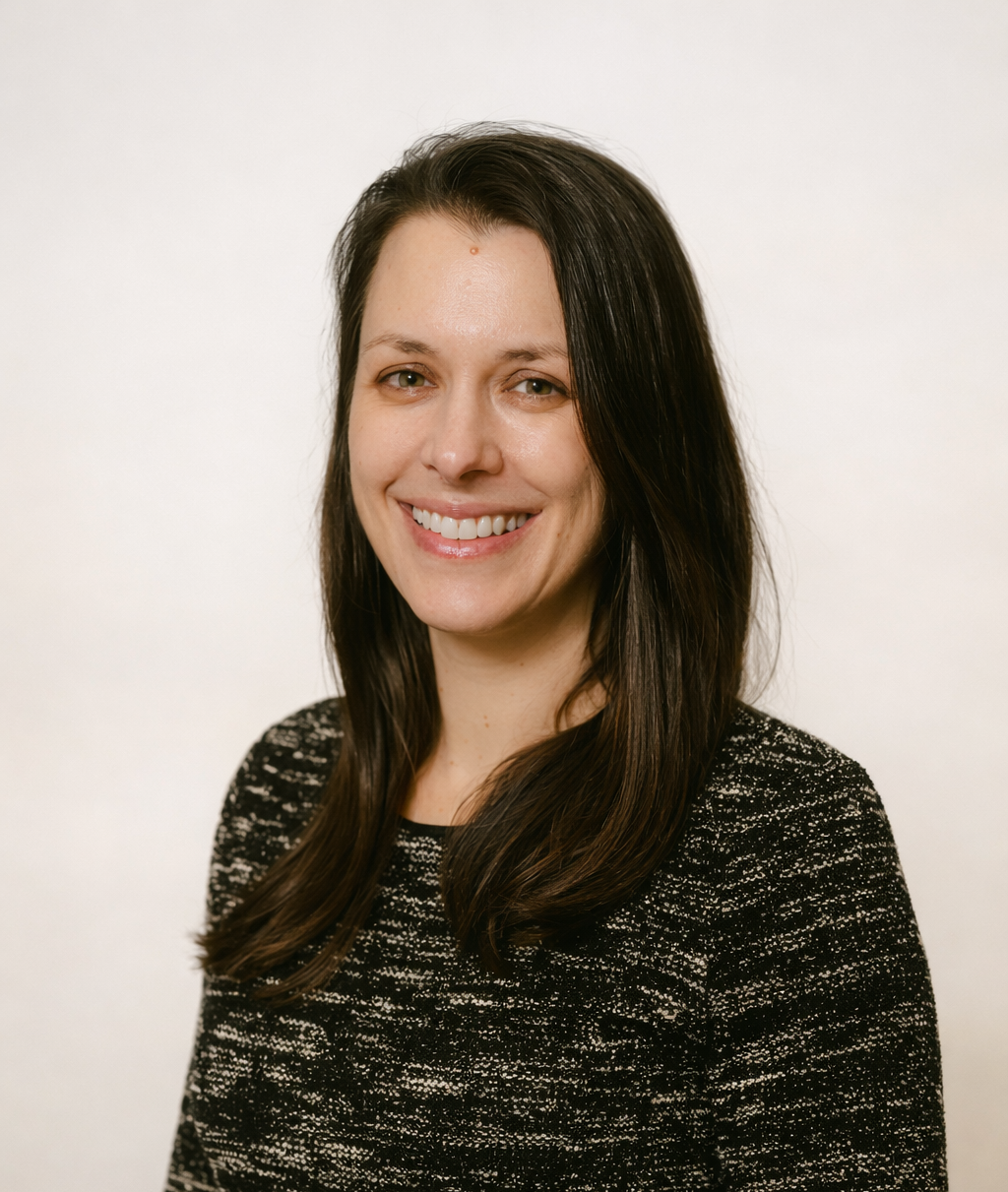 Portrait of a woman with long dark hair smiling, wearing a black and white textured sweater, against a plain white background.