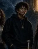 A young man with curly hair wearing a black hoodie standing outdoors at night.