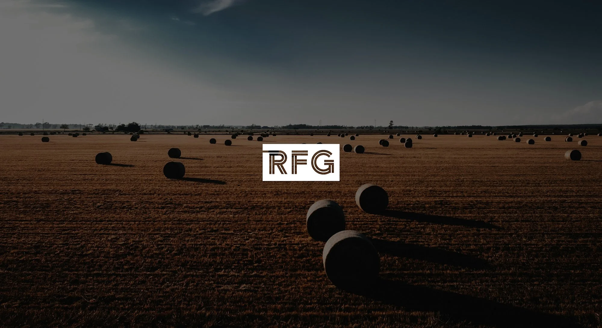 A vast agricultural field with numerous round hay bales scattered across the land under a dark, cloudy sky. The logo 'RFG' is centered in the image.