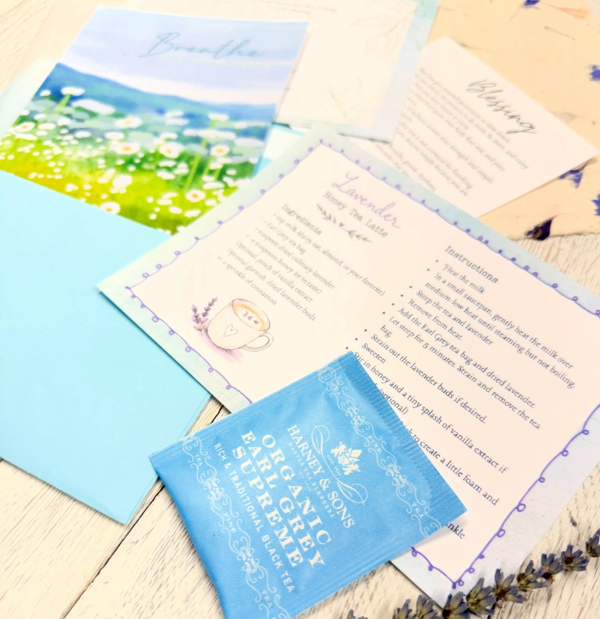 Collection of printed papers and tea bags on a white wooden surface, with some lavender flowers nearby, including a tea bag with a blue and white design.