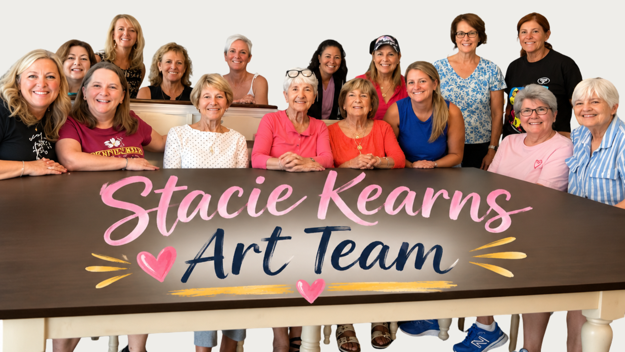 Group of women and girls gathered around a table with a sign saying 'Stacie Kearns Art Team' in pink, blue, and yellow lettering, decorated with hearts and lines.