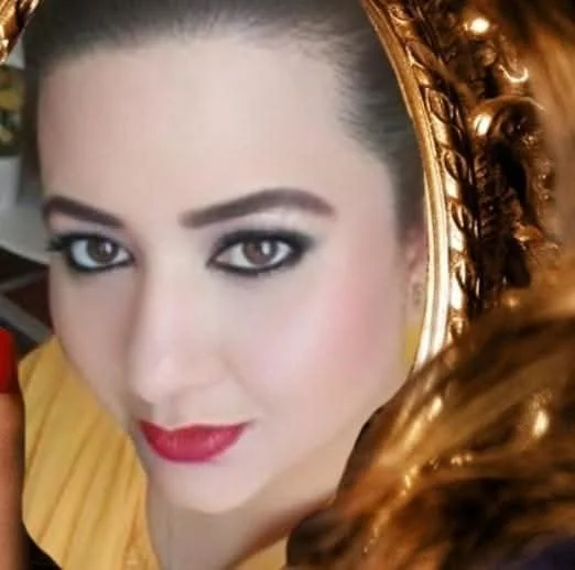 A woman with dark eye makeup, red lipstick, and dark hair styled with golden accessories.