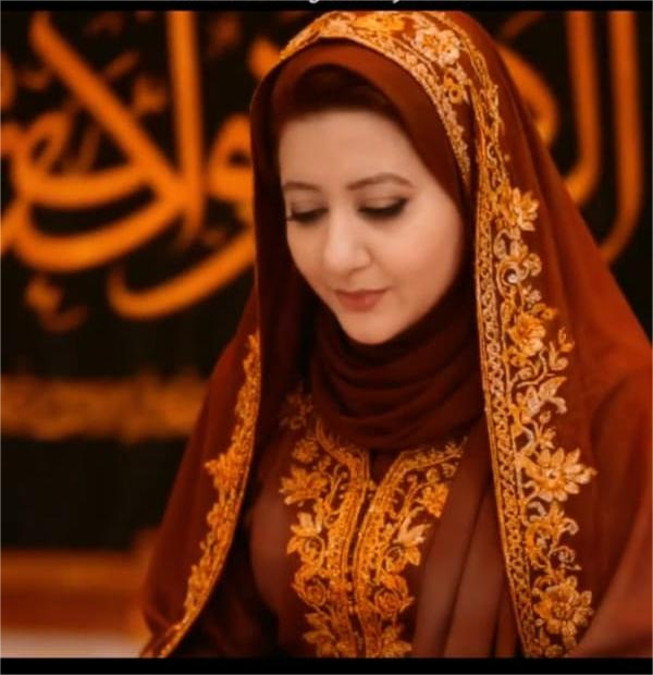 A woman dressed in a traditional brown and gold embroidered outfit and a headscarf, looking down thoughtfully.