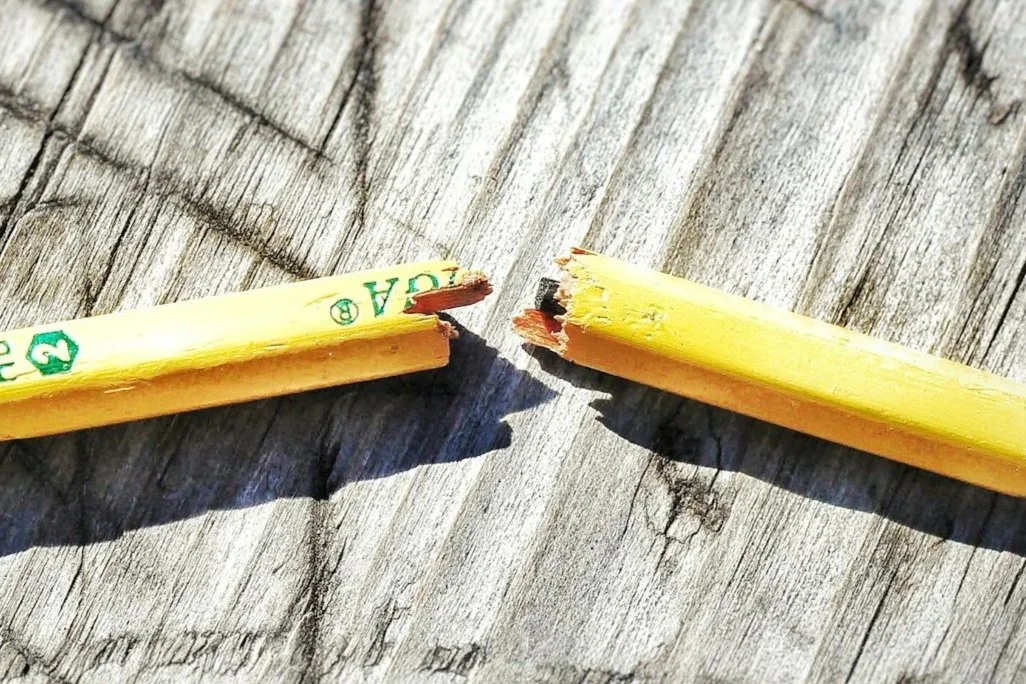 A close-up of a broken pencil on a scratched wooden background.