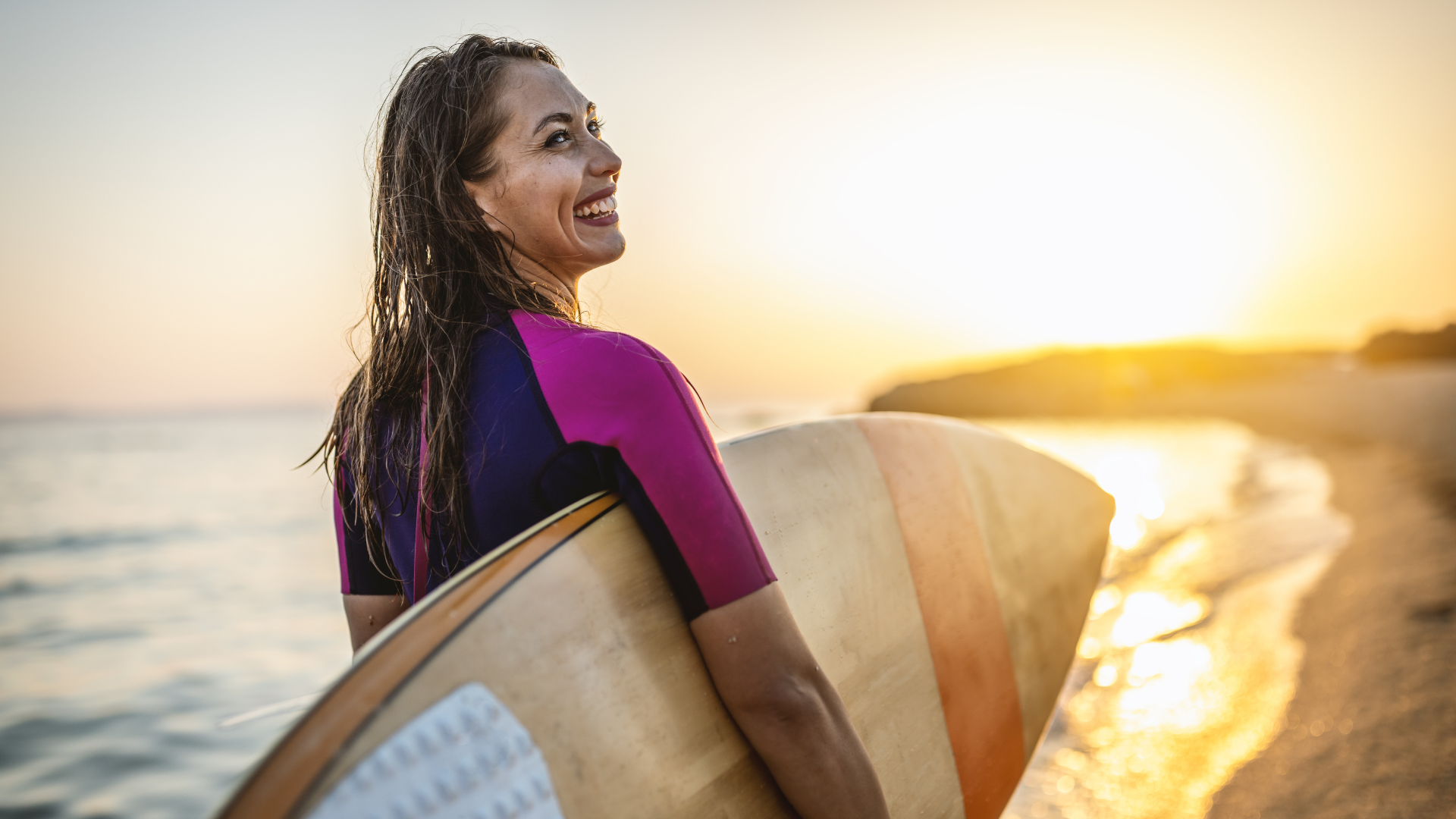 woman in water, smiling while holding her surf board