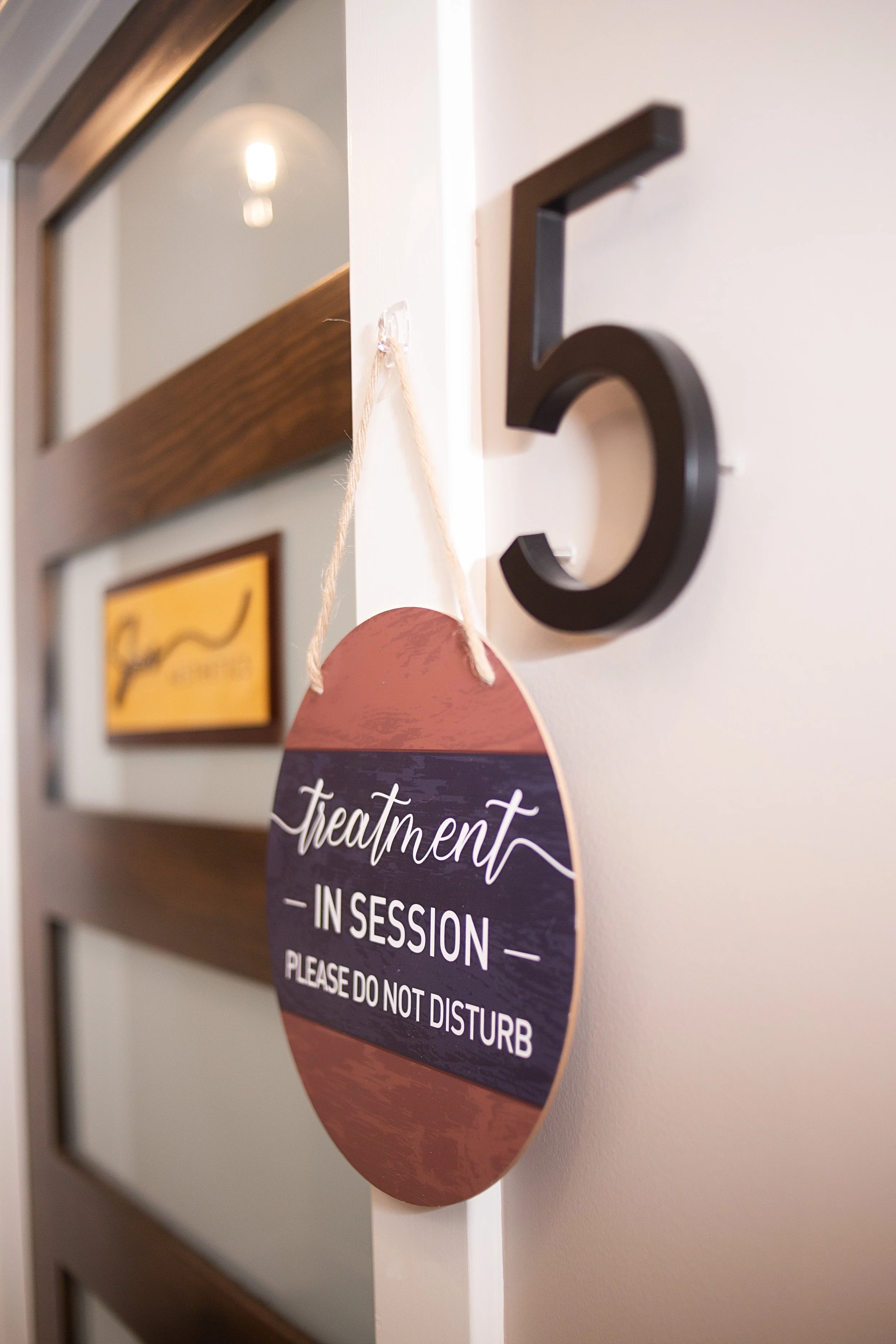 A wall with framed pictures and a round sign that reads 'Treatment in progress - Please do not disturb' in large white text on a purple background.