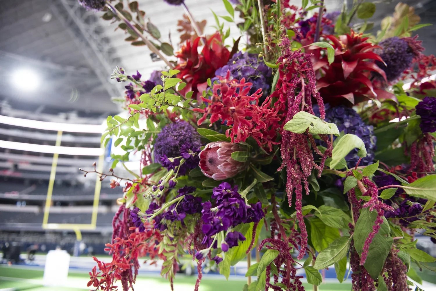 Colorful bouquet of purple, pink, and red flowers with green leaves in a stadium setting.