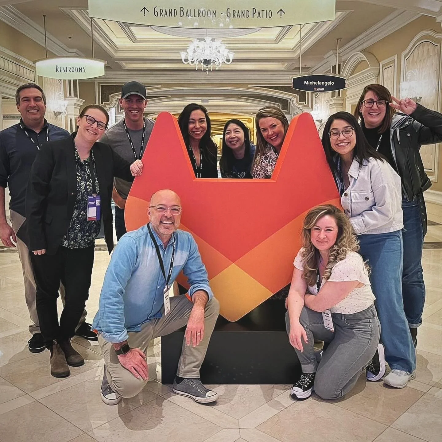 Vic Bell with her GitLab teammates at GitLab Summit, posing together beside a large GitLab logo sculpture.