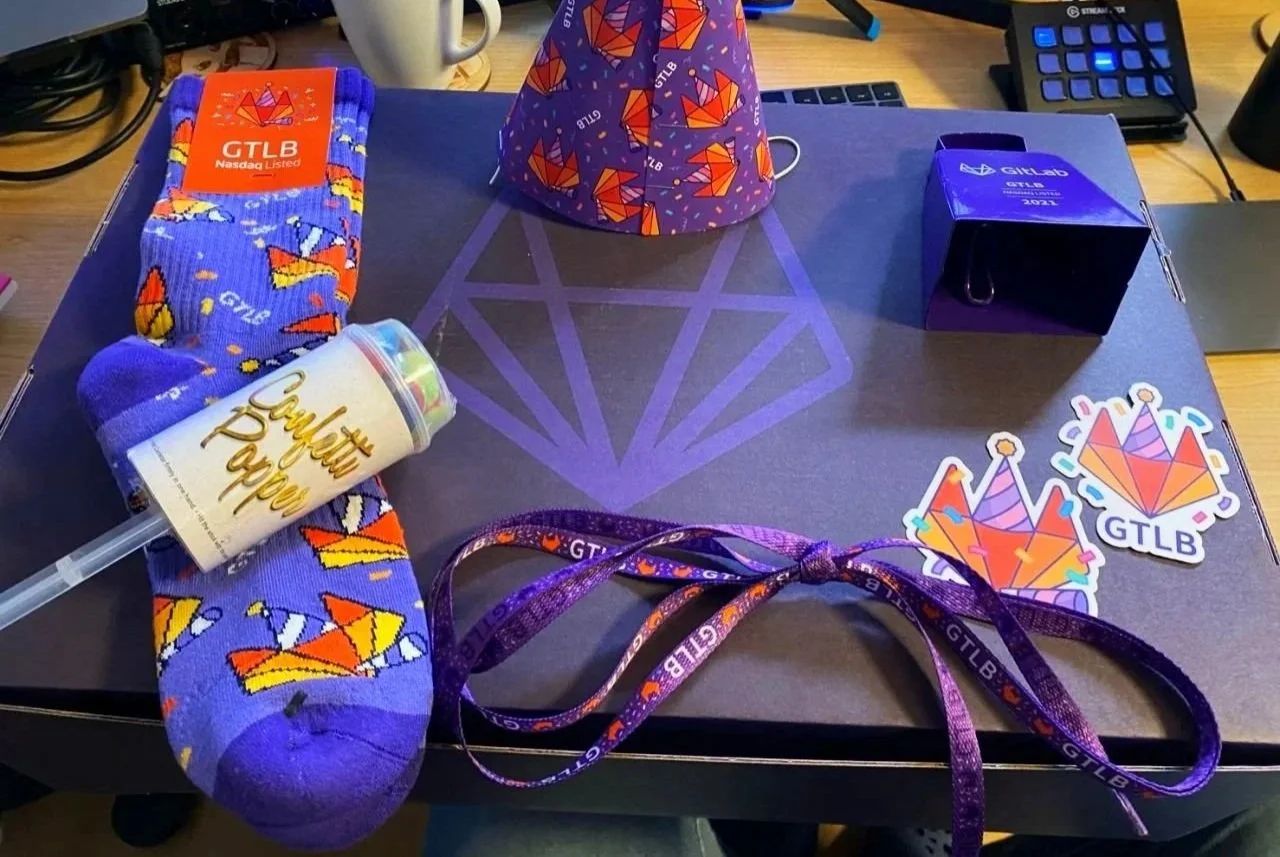 GitLab IPO celebration gift box featuring custom illustrated merchandise, branded socks, stickers, a party hat and other commemorative items celebrating the company's Nasdaq listing.